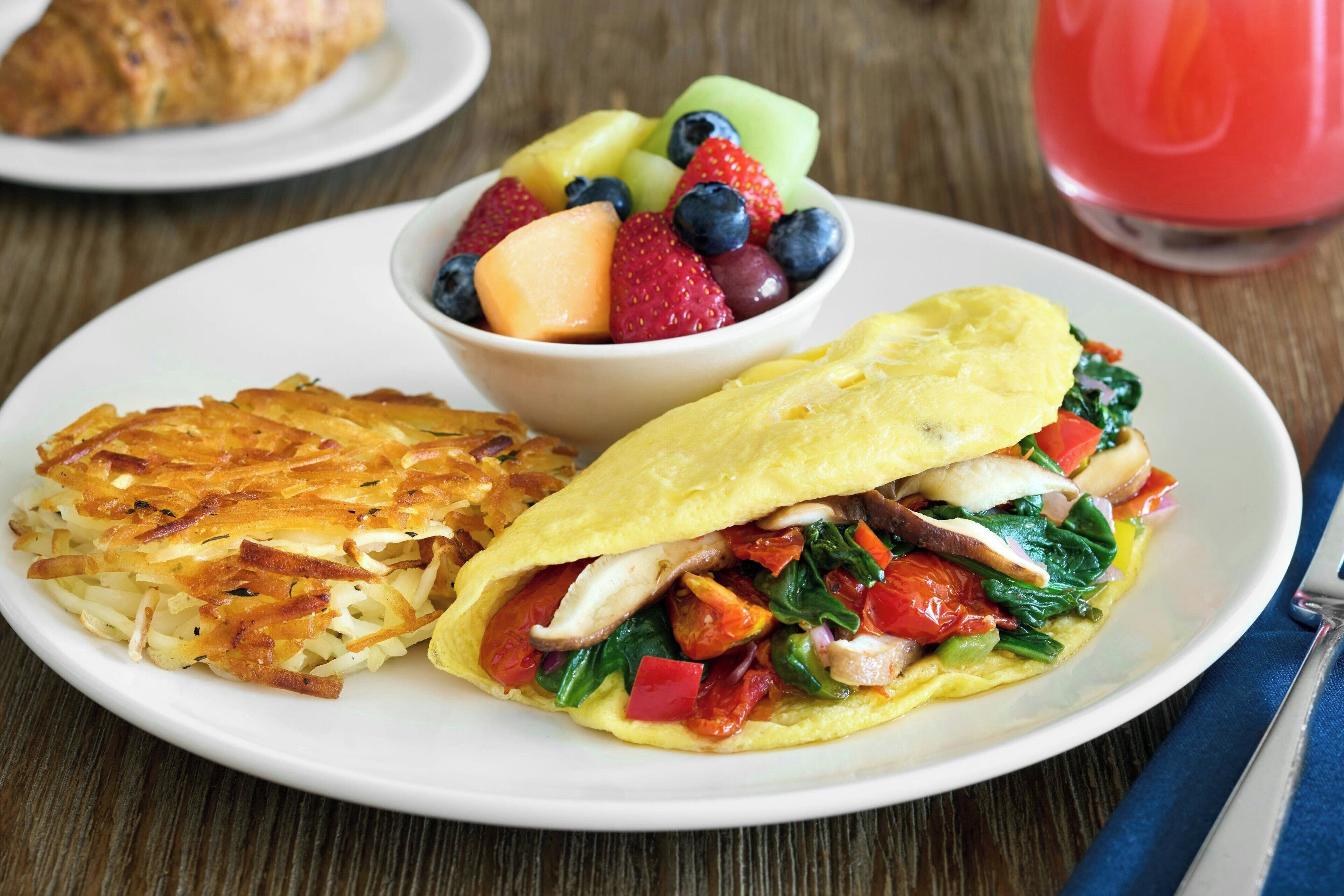 A plate with an omelette, hash browns, and a fruit bowl.
