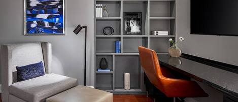 A modern living room with a grey sofa, a matching ottoman, a red chair, a bookshelf, and a flat-screen TV.