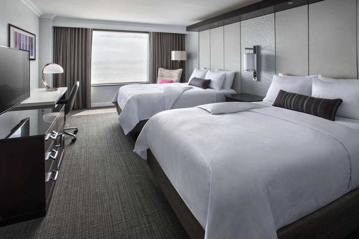 Een hotelkamer met twee bedden, een bureau, een stoel, een televisie en een groot raam met gordijnen.