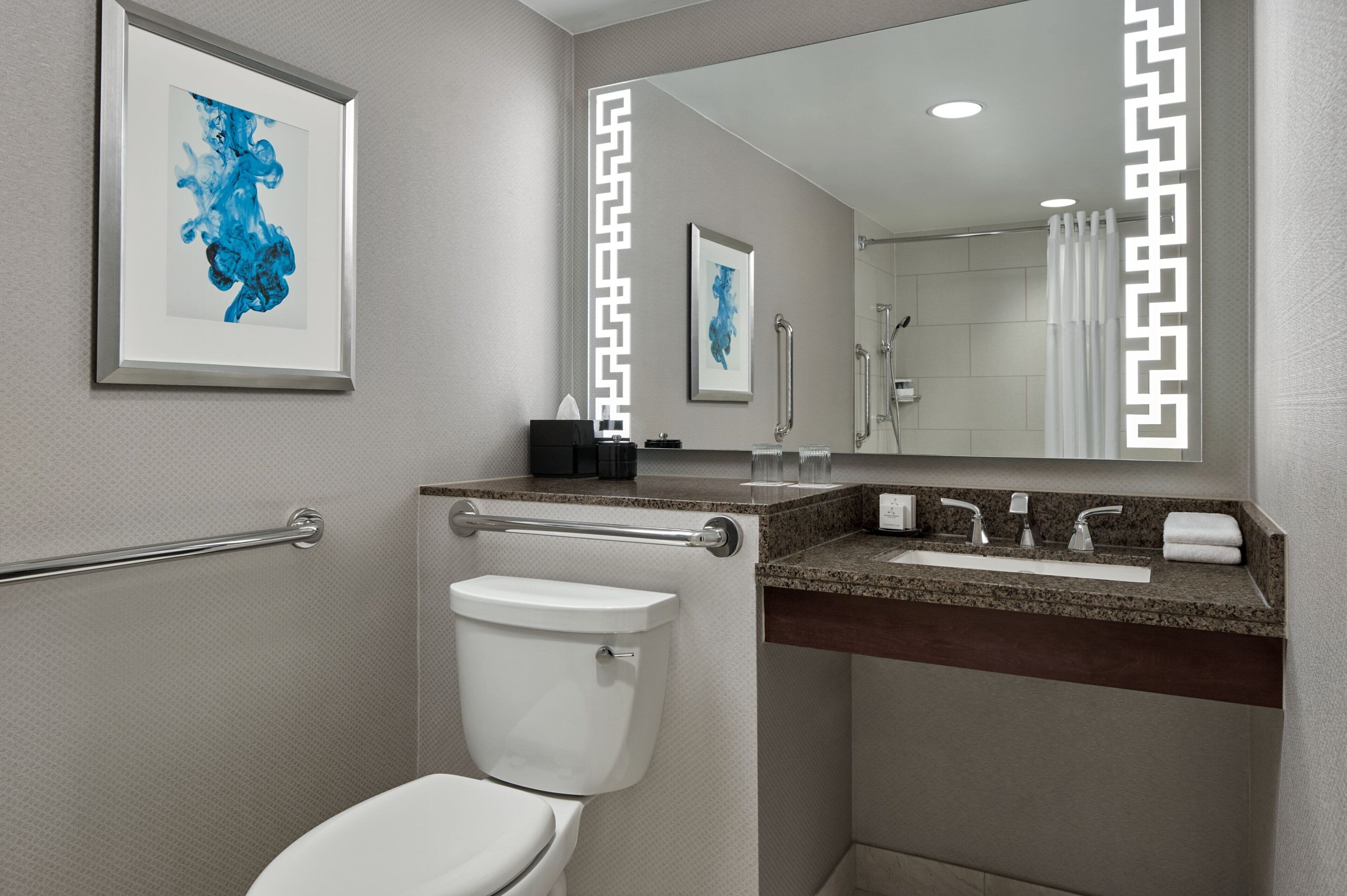 Ein modernes Badezimmer mit Toilette, Waschbecken und Dusche. An den Wänden befinden sich gerahmte Kunstwerke und ein Spiegel mit Zierrahmen.