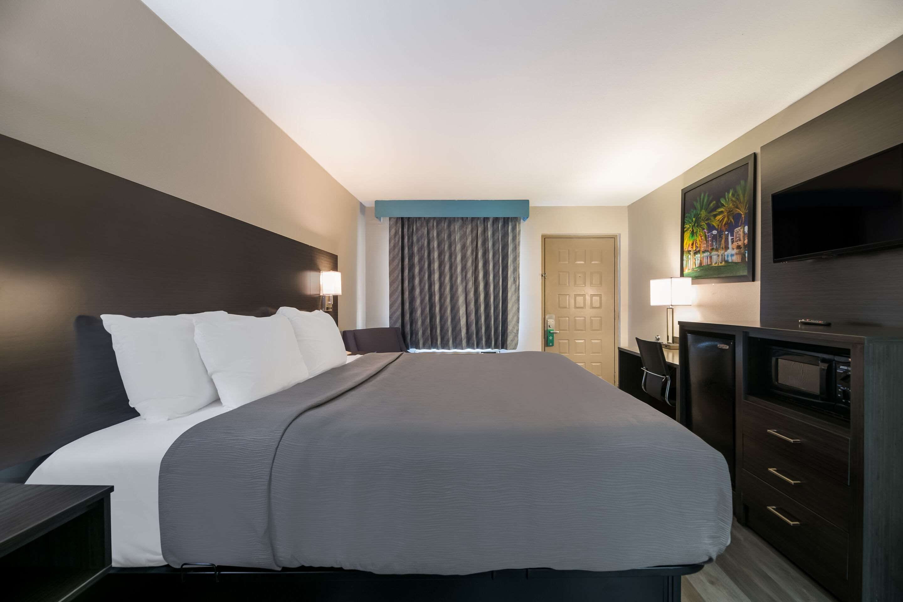 A hotel room with a large bed, a desk, a TV, and a door.