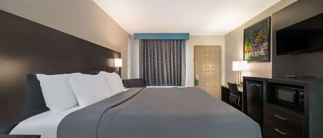 A hotel room with a large bed, a desk, a TV, and a door.