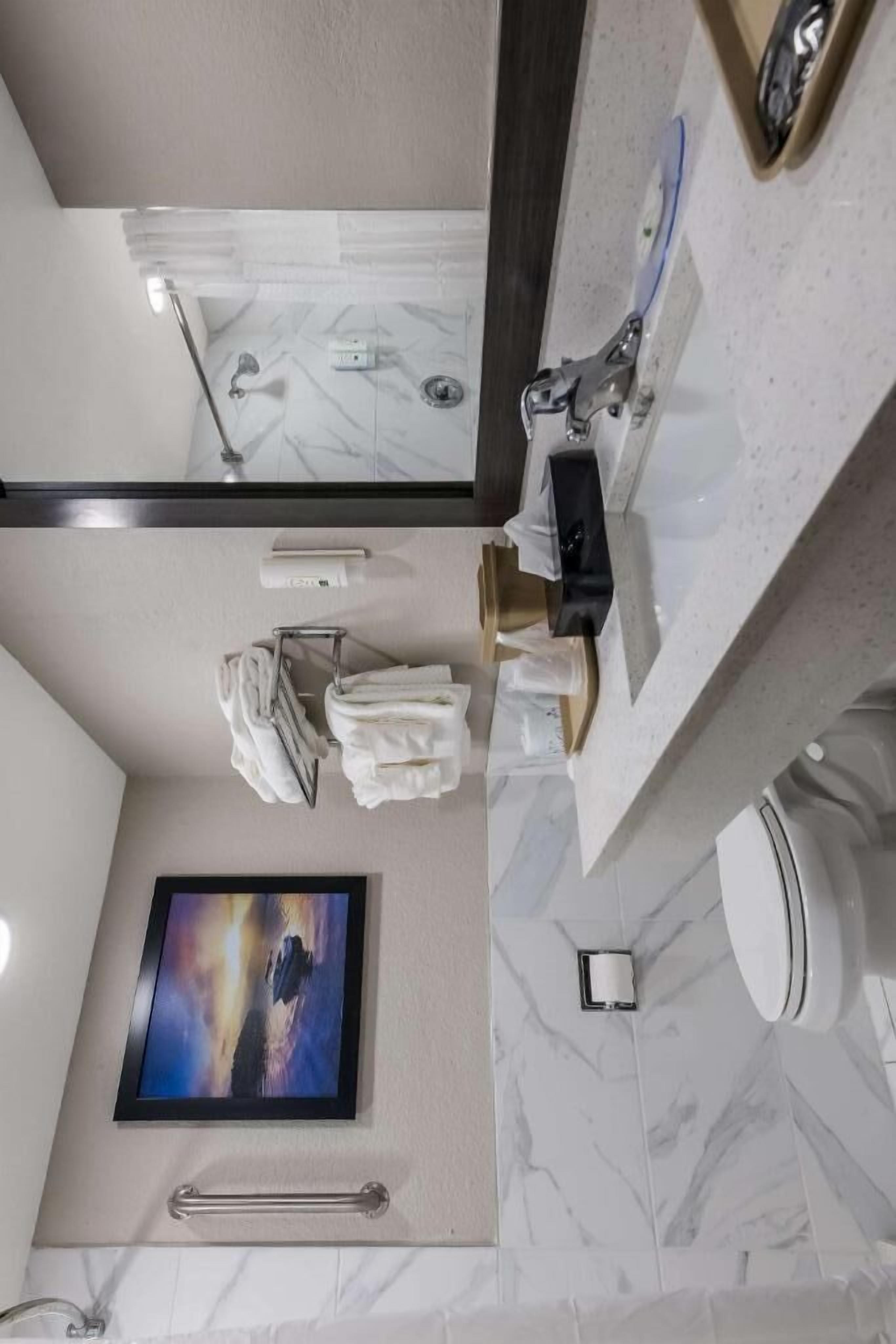 Un baño con piso de mármol, un lavamanos con espejo, toallero, inodoro y un cuadro en la pared.