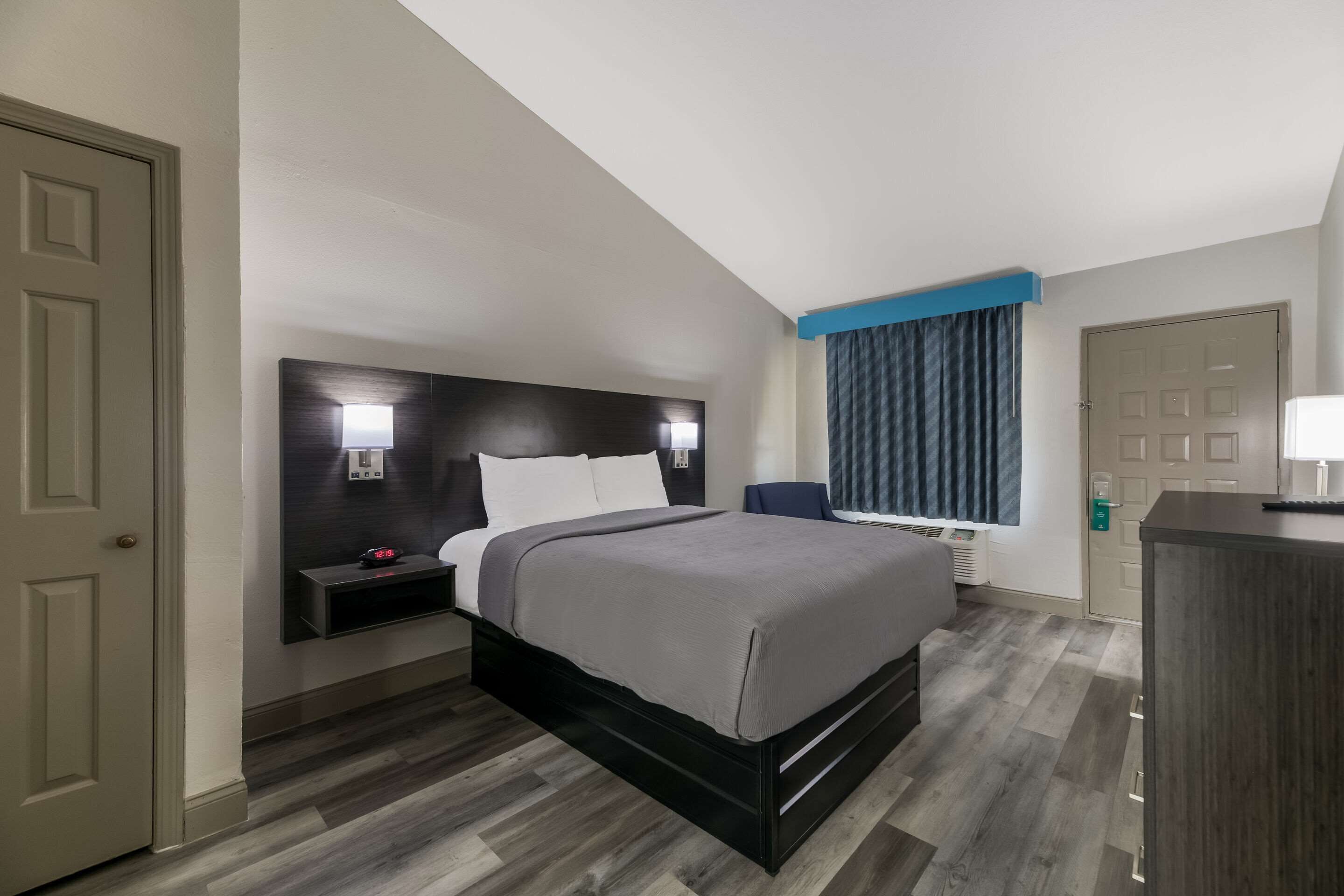 A modern hotel room with a large bed, a bedside table, a desk, and a window with curtains.