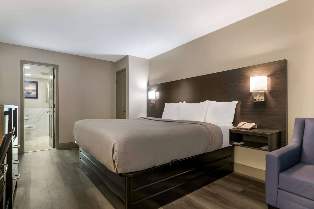 Quarto de hotel com cama, mesa de cabeceira, cadeira e porta para o banheiro.