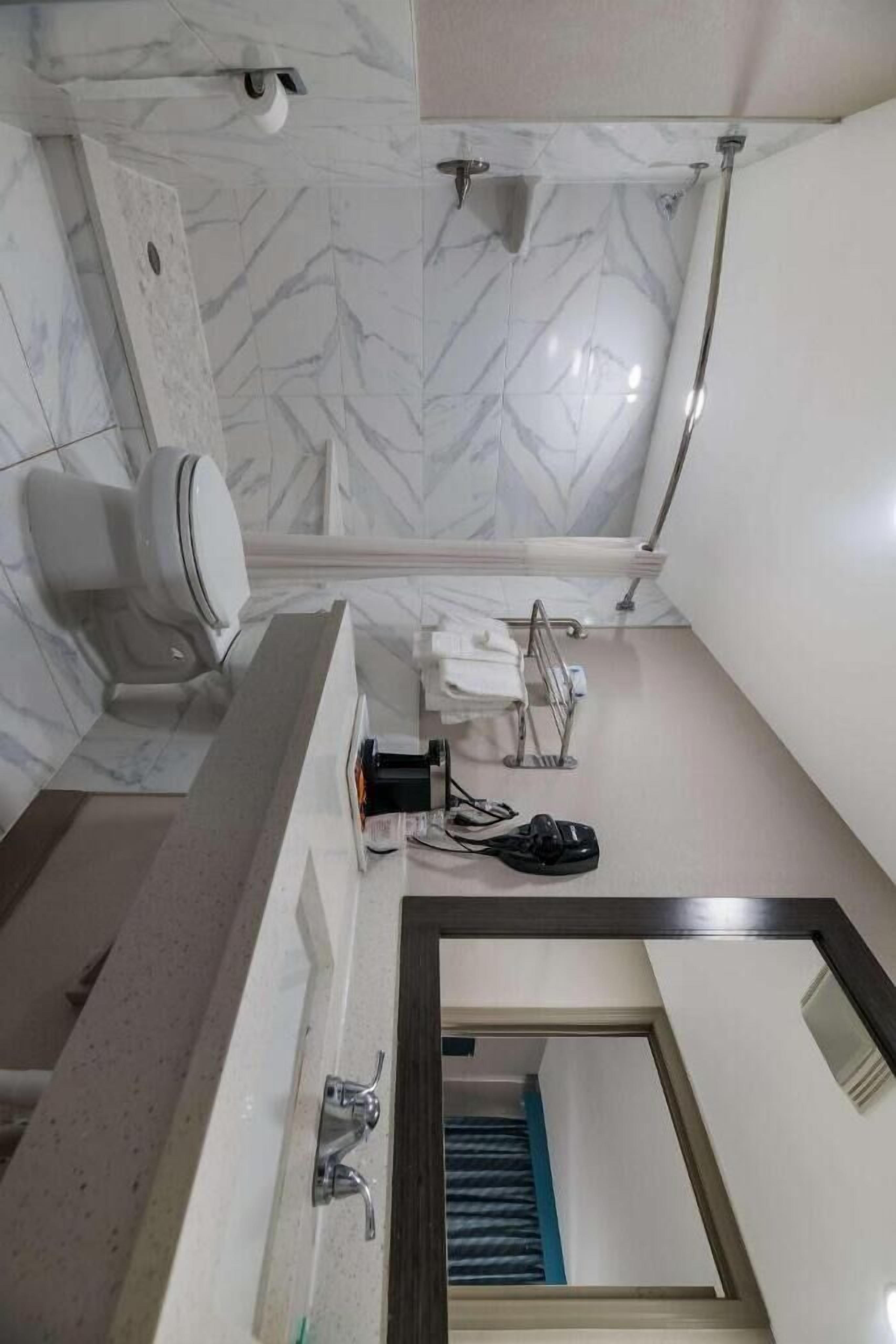 A bathroom with a marble floor, a sink, a mirror, a towel rack, a shower, and a toilet.