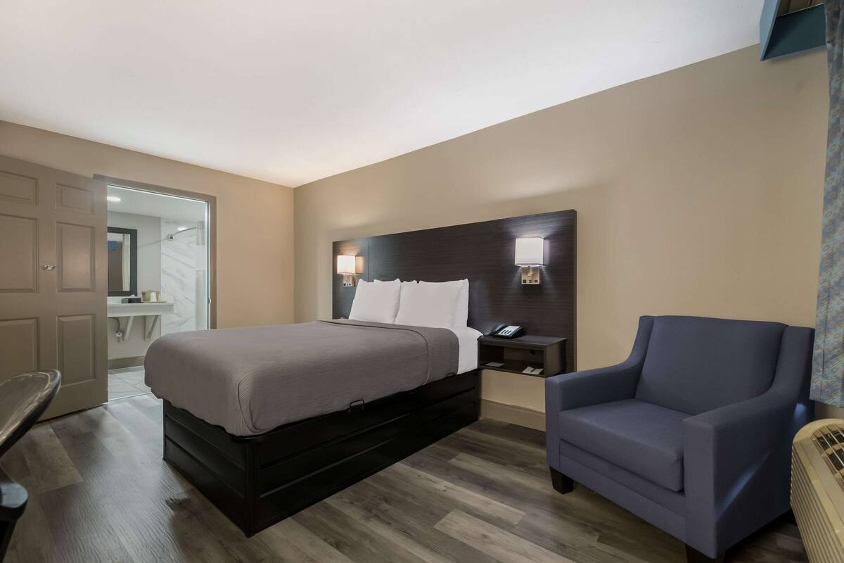 Quarto de hotel com cama, mesa de cabeceira, cadeira e vista para o banheiro.