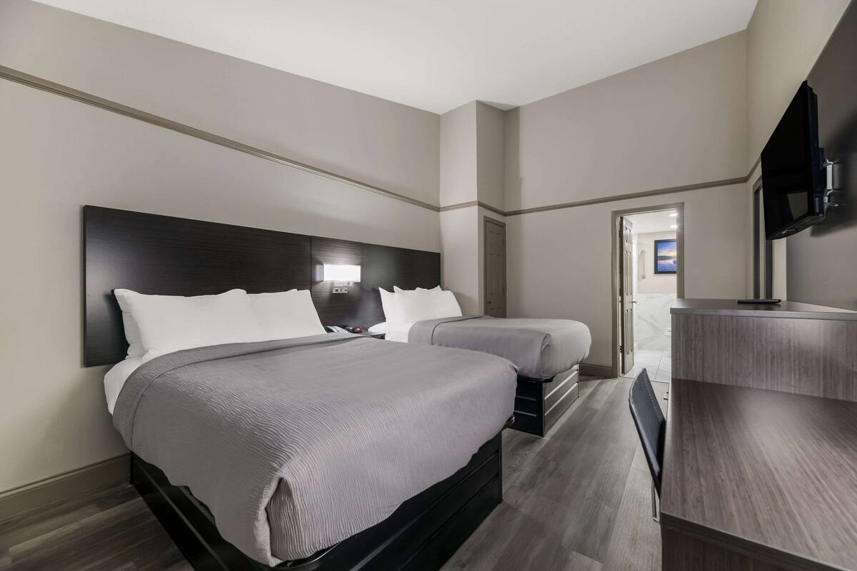 Quarto de hotel com uma cama grande, uma cama menor, uma escrivaninha e uma televisão.