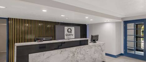 A hotel reception desk with a marble counter, a sign reading "Quality by Choice Hotel," and a computer monitor.