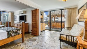 A hotel room with a bed, a sofa, a TV, a wooden cabinet, and a balcony with a view of the city. - Castle Bamboo Waikīkī Hotel (Honolulu)