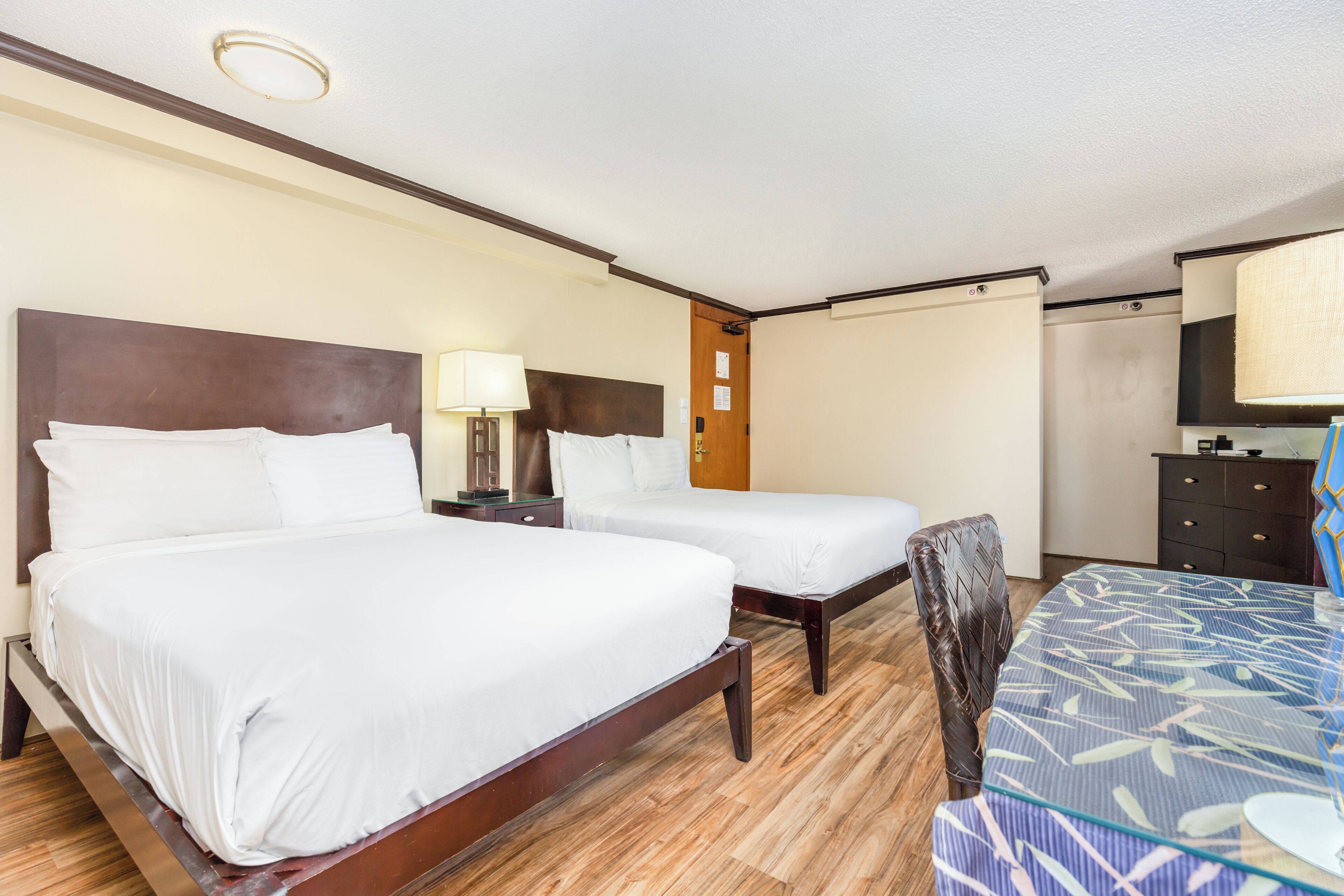 A hotel room with two beds, a desk, a chair, and a dresser.