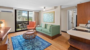 A modern hotel room with a green sofa, a wooden dining table, a kitchen area, and a balcony with a view of the city. - Castle Bamboo Waikīkī Hotel (Honolulu)
