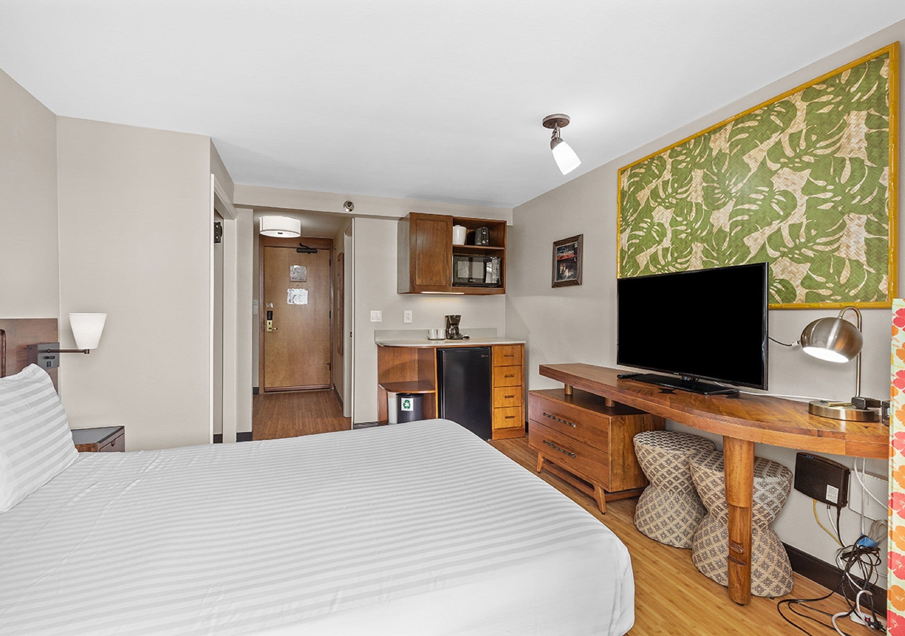 Ein Hotelzimmer mit Bett, Schreibtisch mit Fernseher, einer kleinen Küchenzeile und einem Badezimmer.