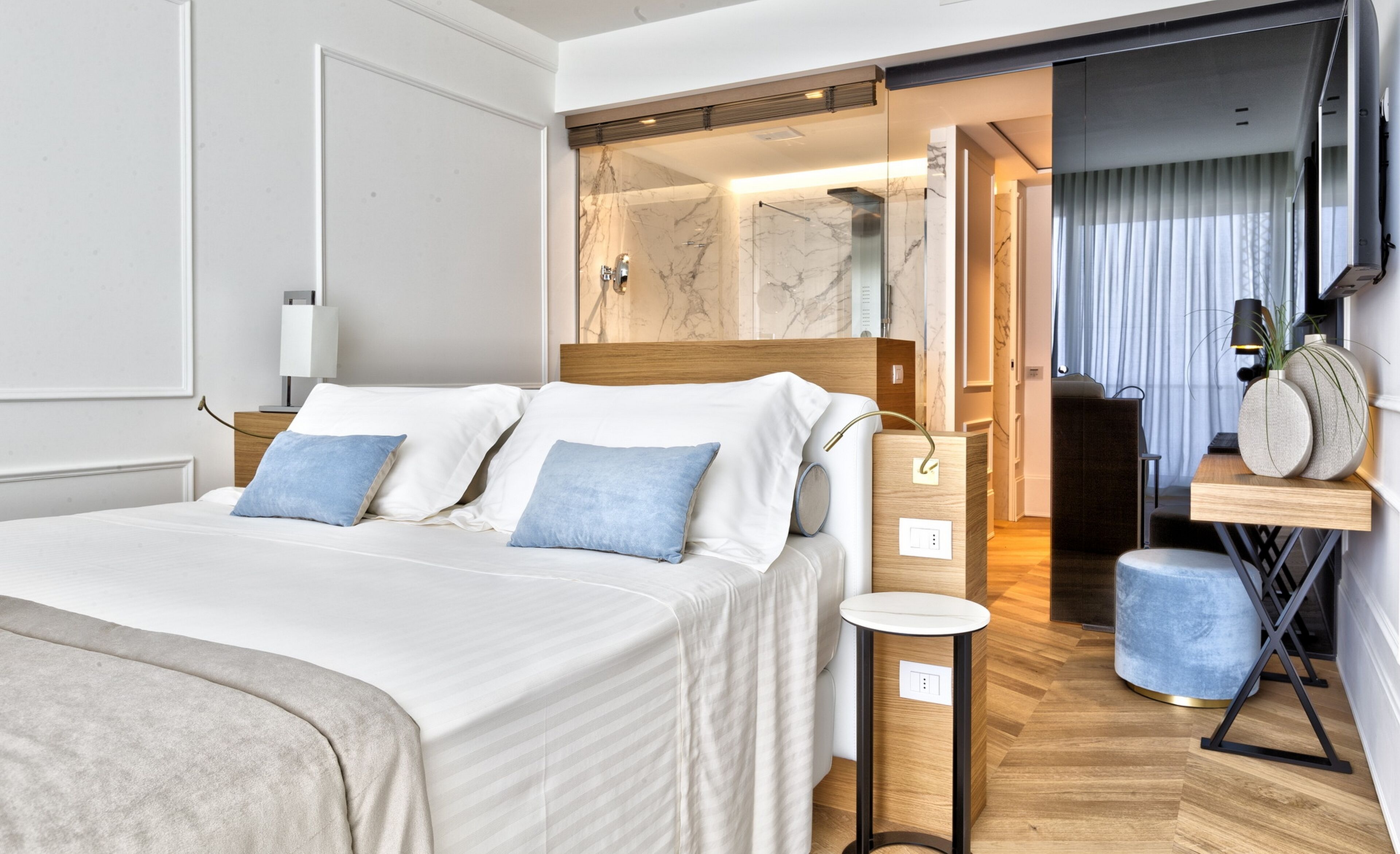 Une chambre d’hôtel moderne avec un grand lit, une table de chevet, un miroir et une petite table ronde.