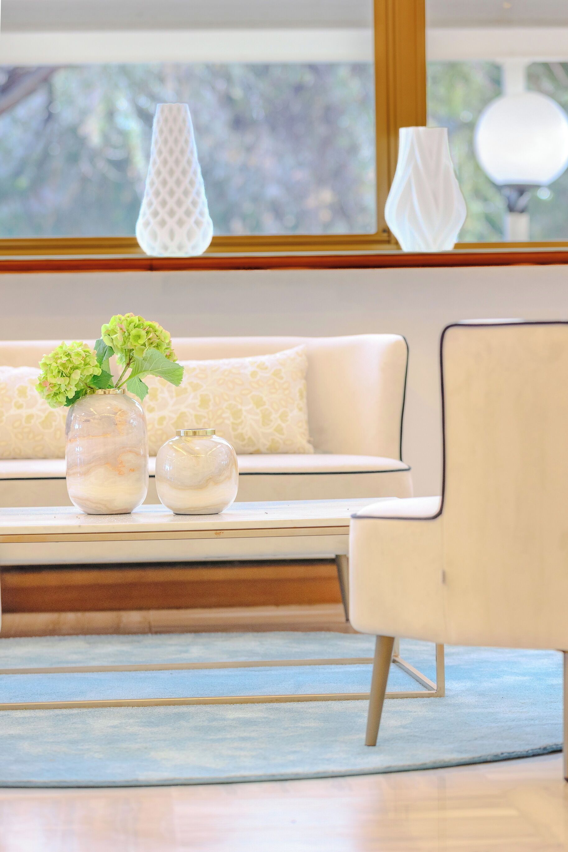 Una sala de estar moderna con un sofá, dos jarrones con flores y un sillón.