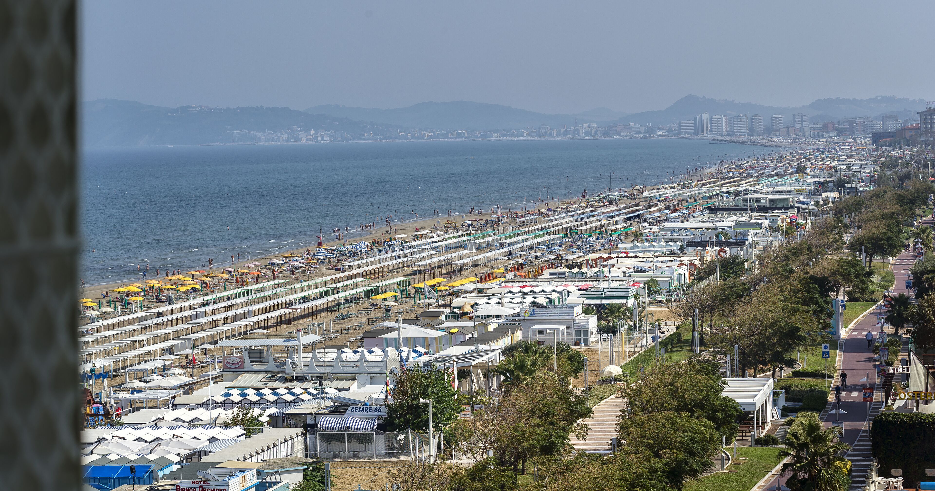 A coastal hotel area with multiple rows of beachside rooms, a promenade, and a view of the sea.