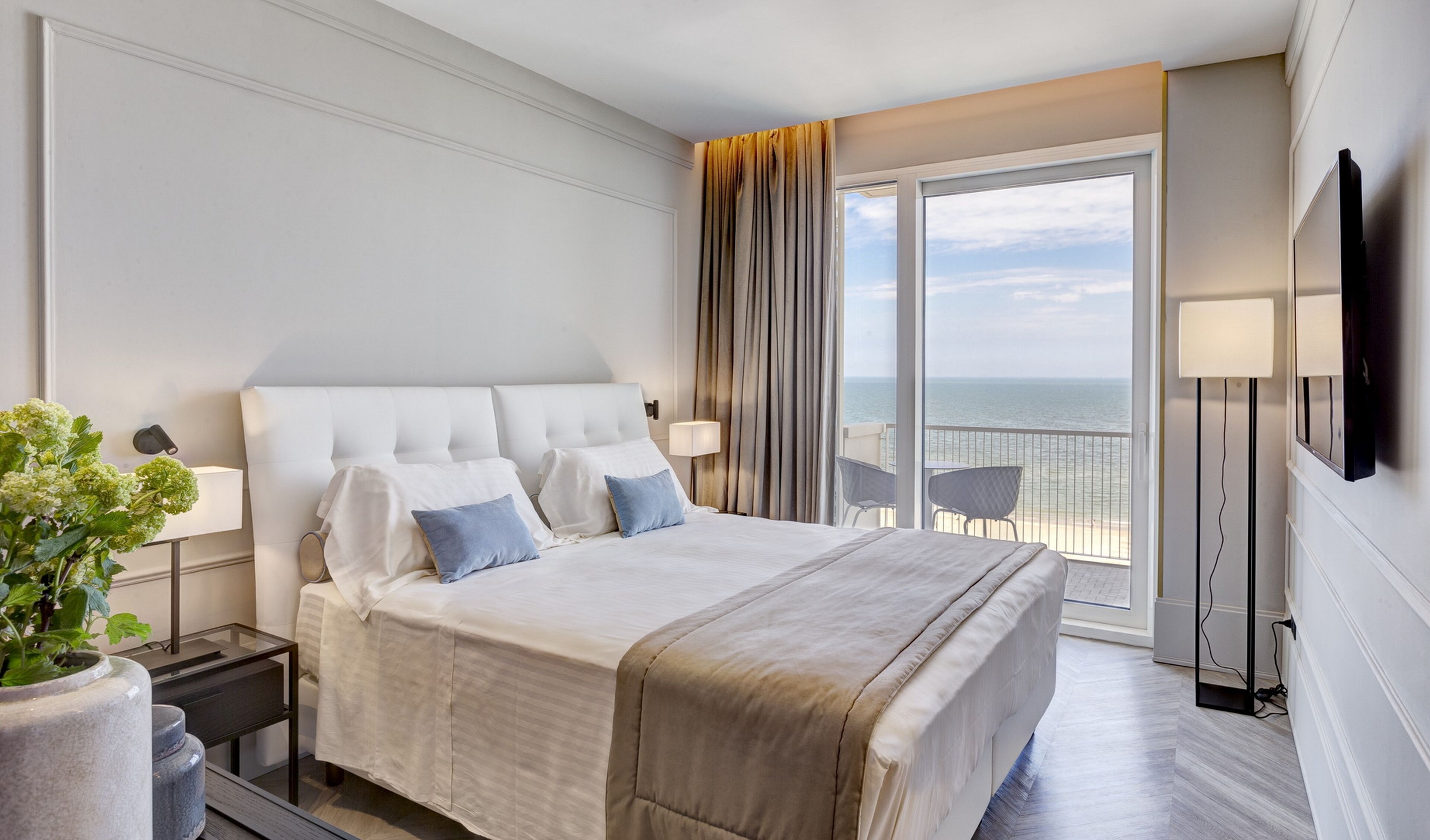 Habitació d'hotel amb un llit gran, un balcó amb vista al mar, un televisió de pantalla plana i una planta en test.