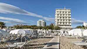 A beachside hotel with multiple white umbrellas, sun loungers, and a wooden walkway.