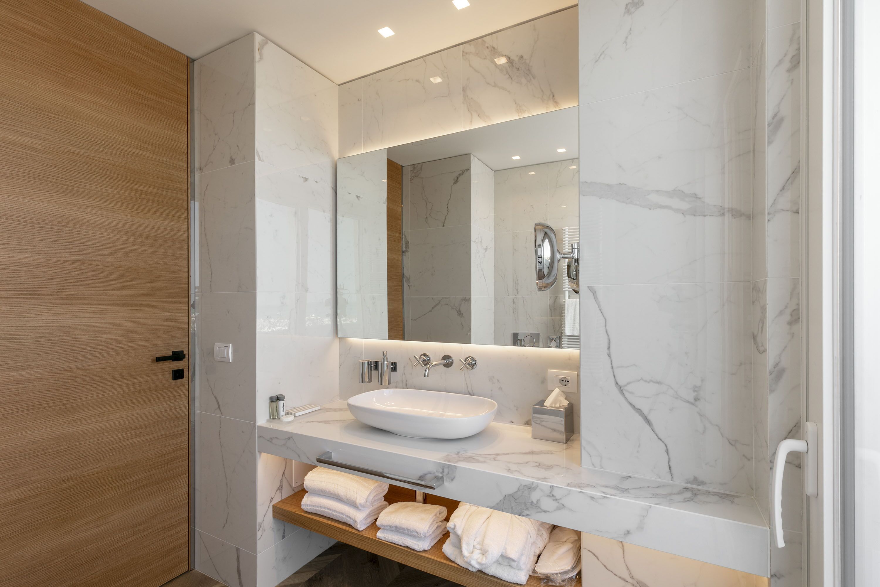 A modern bathroom with a marble sink, wooden door, and a towel rack.