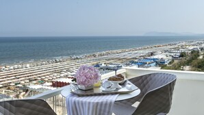 A balcony with a table set for breakfast overlooking a beach with rows of umbrellas and a view of the sea. - Hotel Abner's (Riccione)
