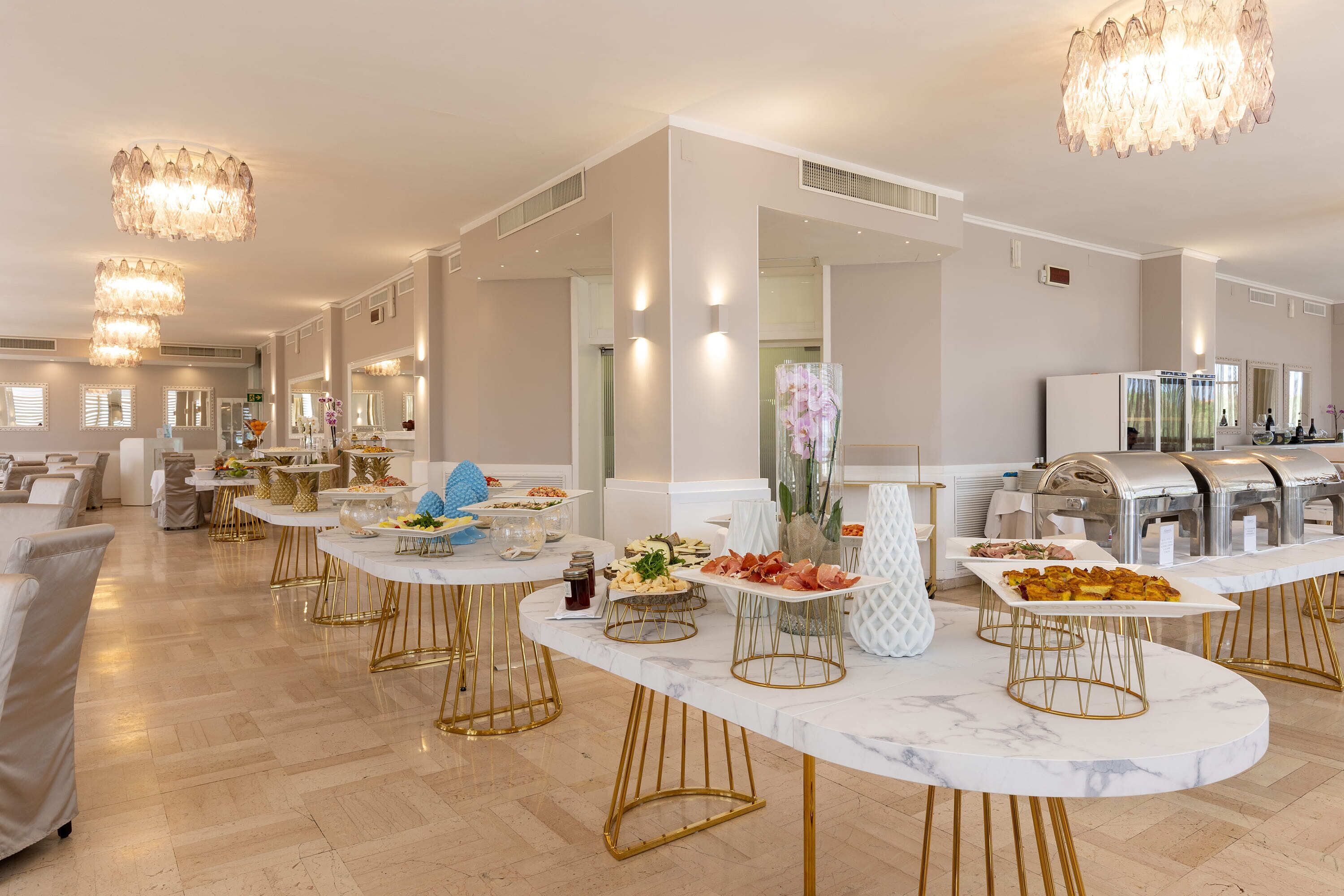 A spacious room with marble tables, gold-legged chairs, and a buffet setup.