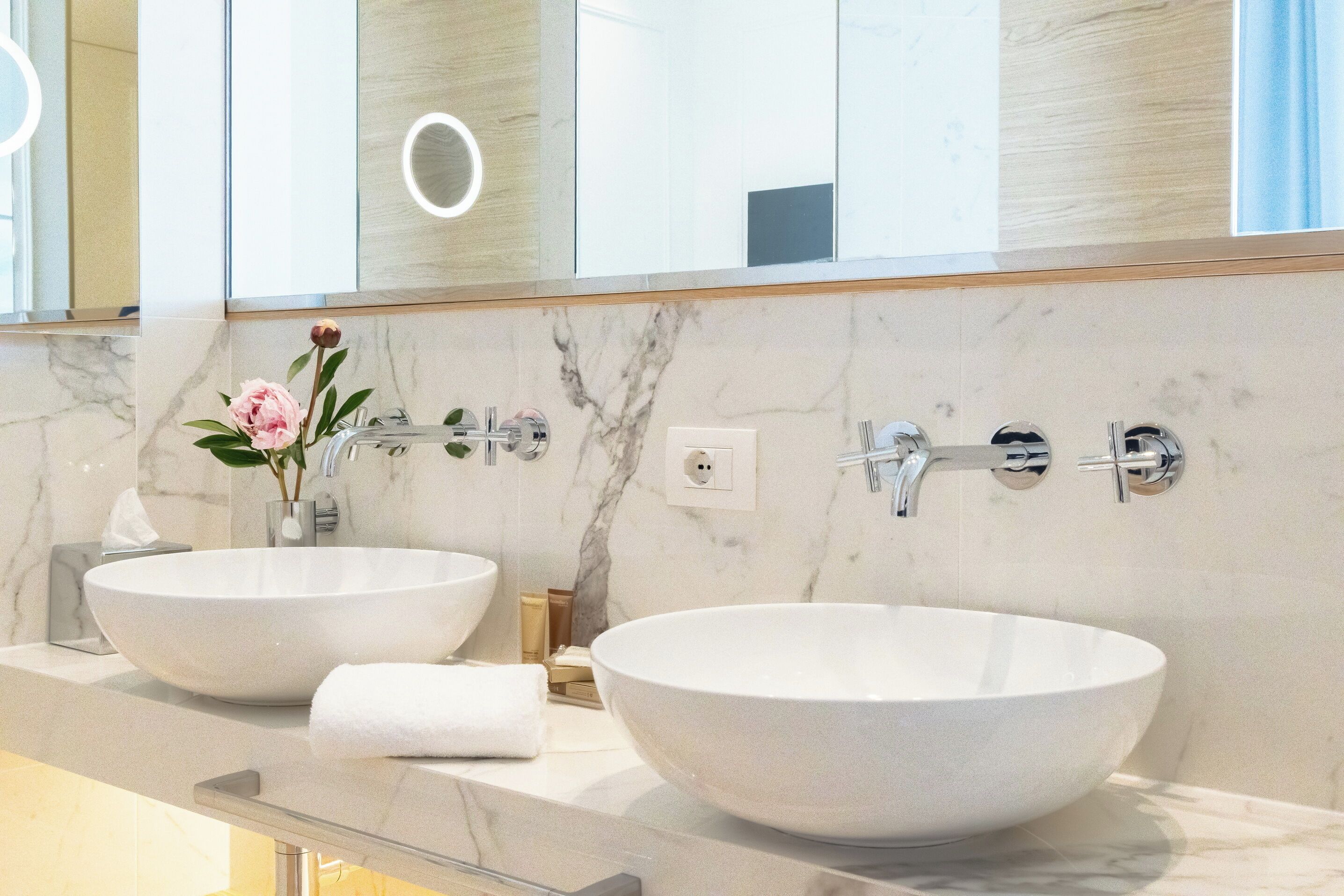 A bathroom with two white vessel sinks, a mirror, and a vase with a flower.