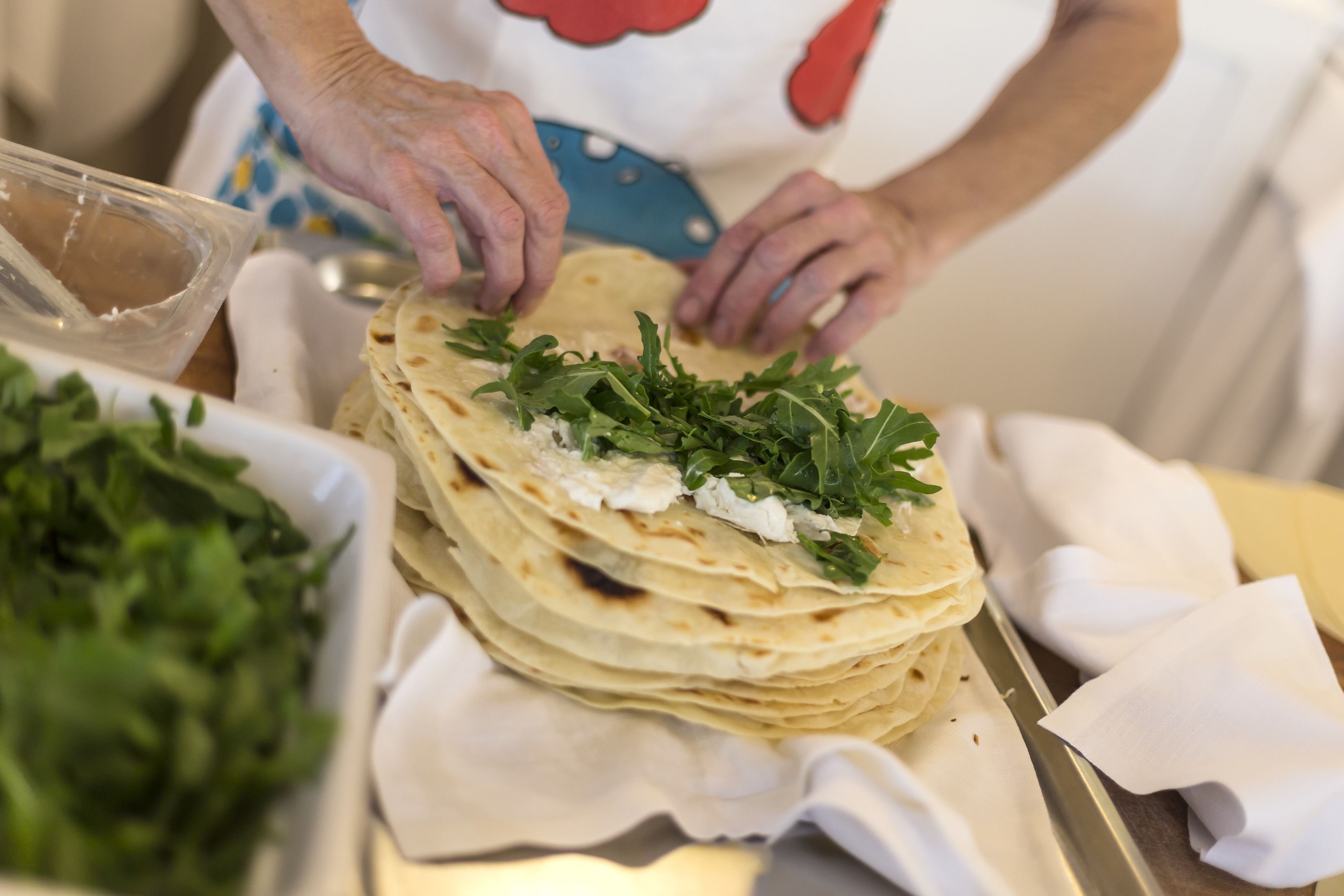 A person preparing a dish with multiple layers of flatbread and fresh greens.