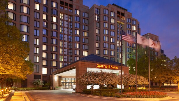 A Marriott Suites hotel with a large building, a well-lit entrance, and a flag.