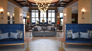 A modern lobby with a central seating area, large windows, and a chandelier.