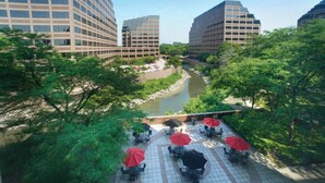 A riverside patio with outdoor seating and a view of modern buildings.