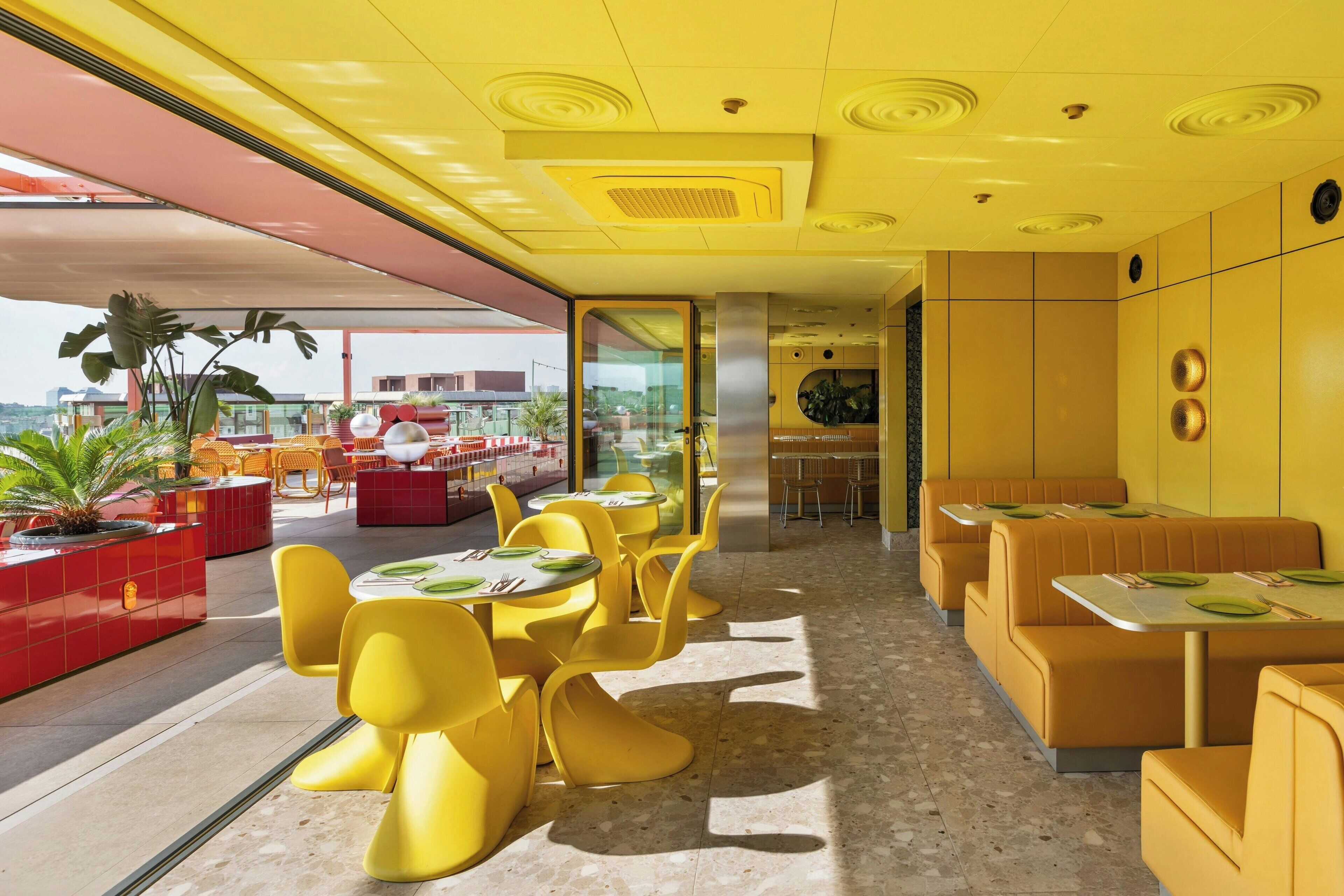 Un restaurant moderne avec des chaises et des tables jaunes, un buffet rouge et une vue sur la ville.