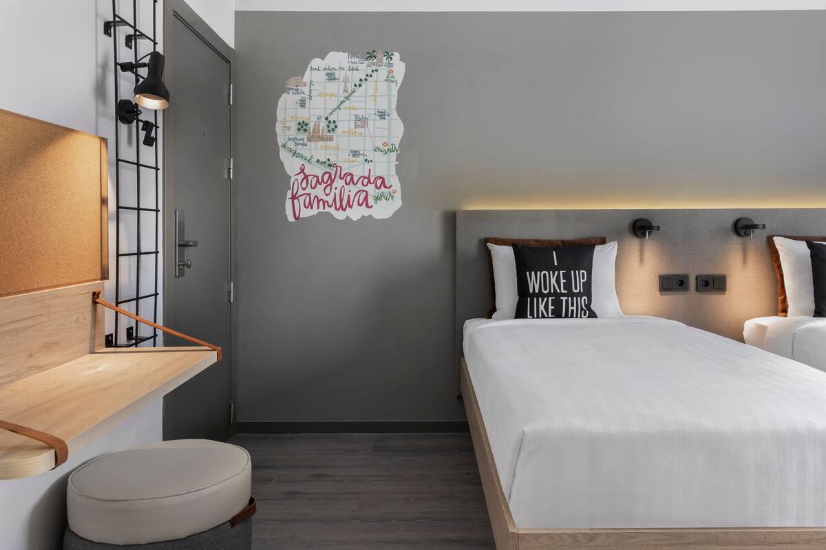 A modern bedroom with a bed, a wall map, and a motivational pillow.