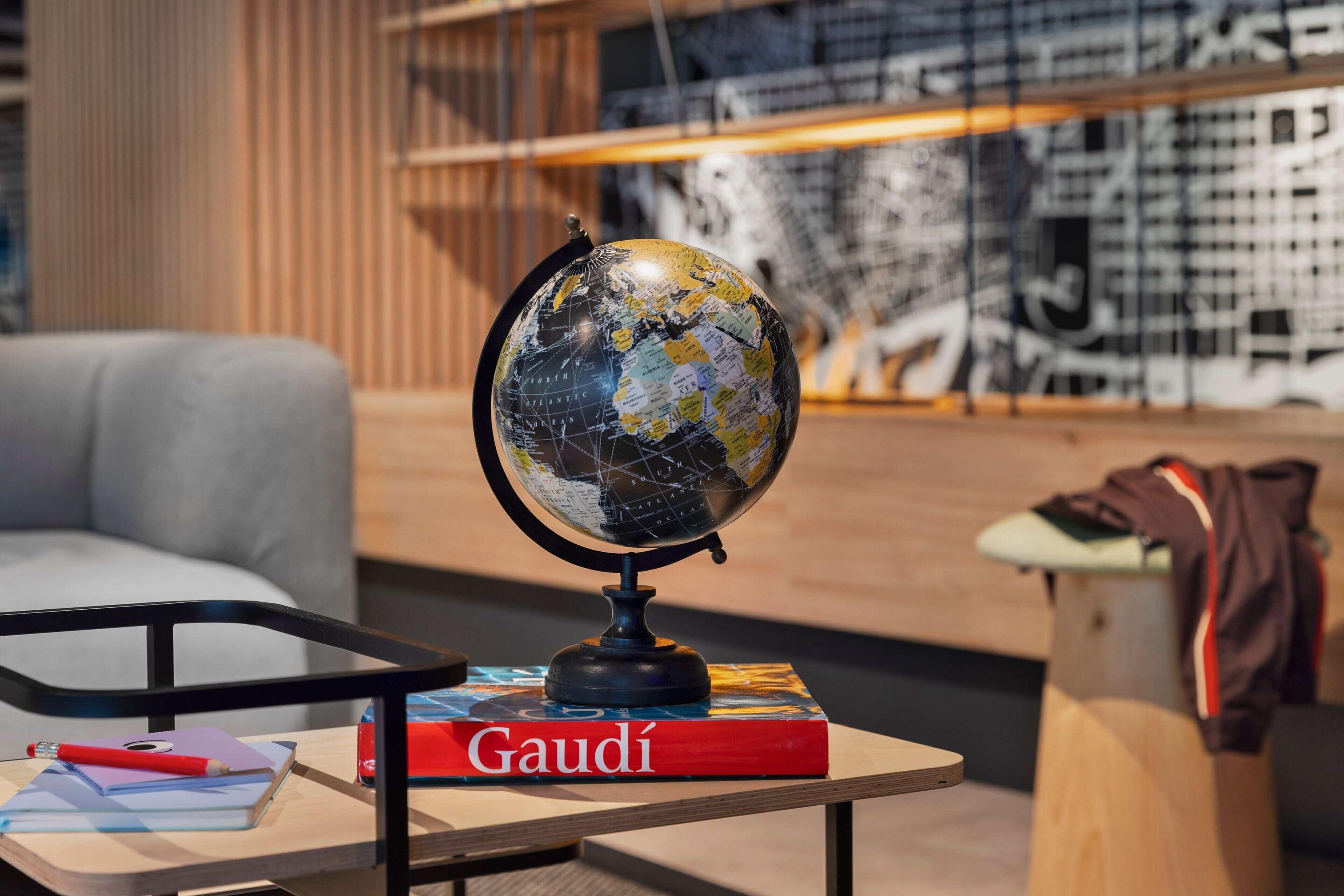 A globe on a table with a book titled "Gaudí" and a red pencil.