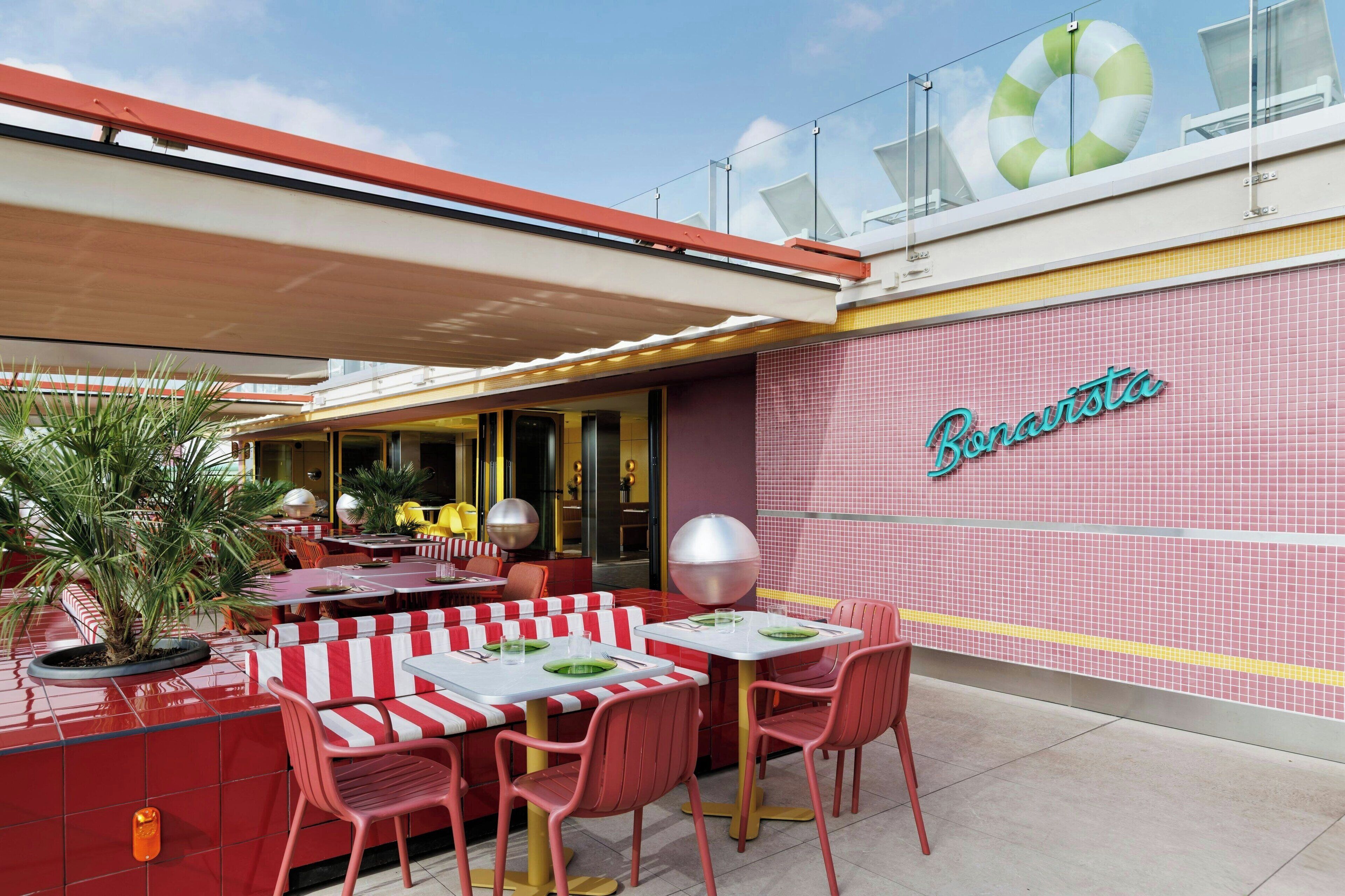 An outdoor seating area with red and white striped booths and tables, a pink tiled wall with the name 'Pinarista', and a lifebuoy decoration on the roof.