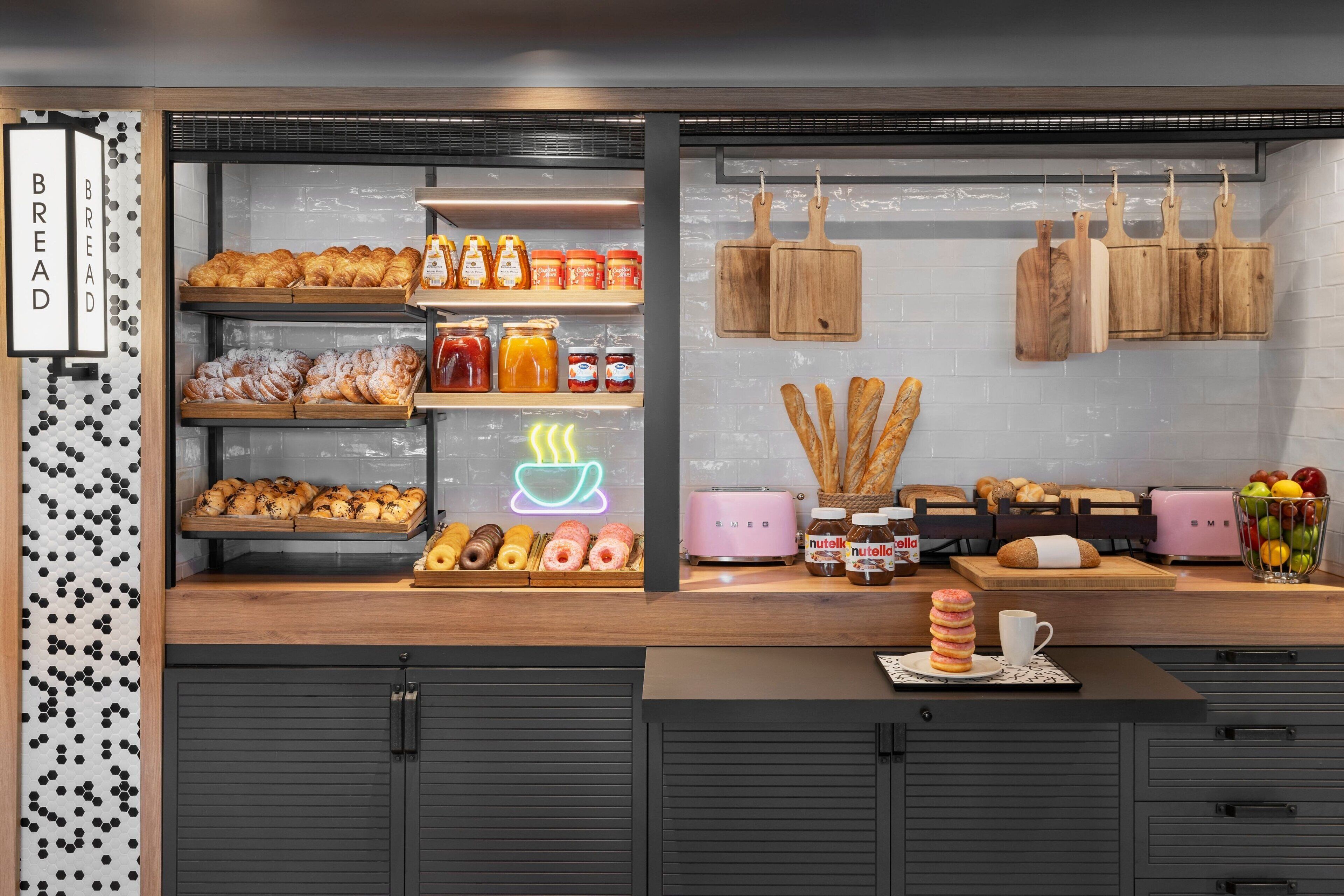 Vitrine de padaria com diversos pães e doces, potes de geleias e um letreiro de neon em formato de xícara de café.