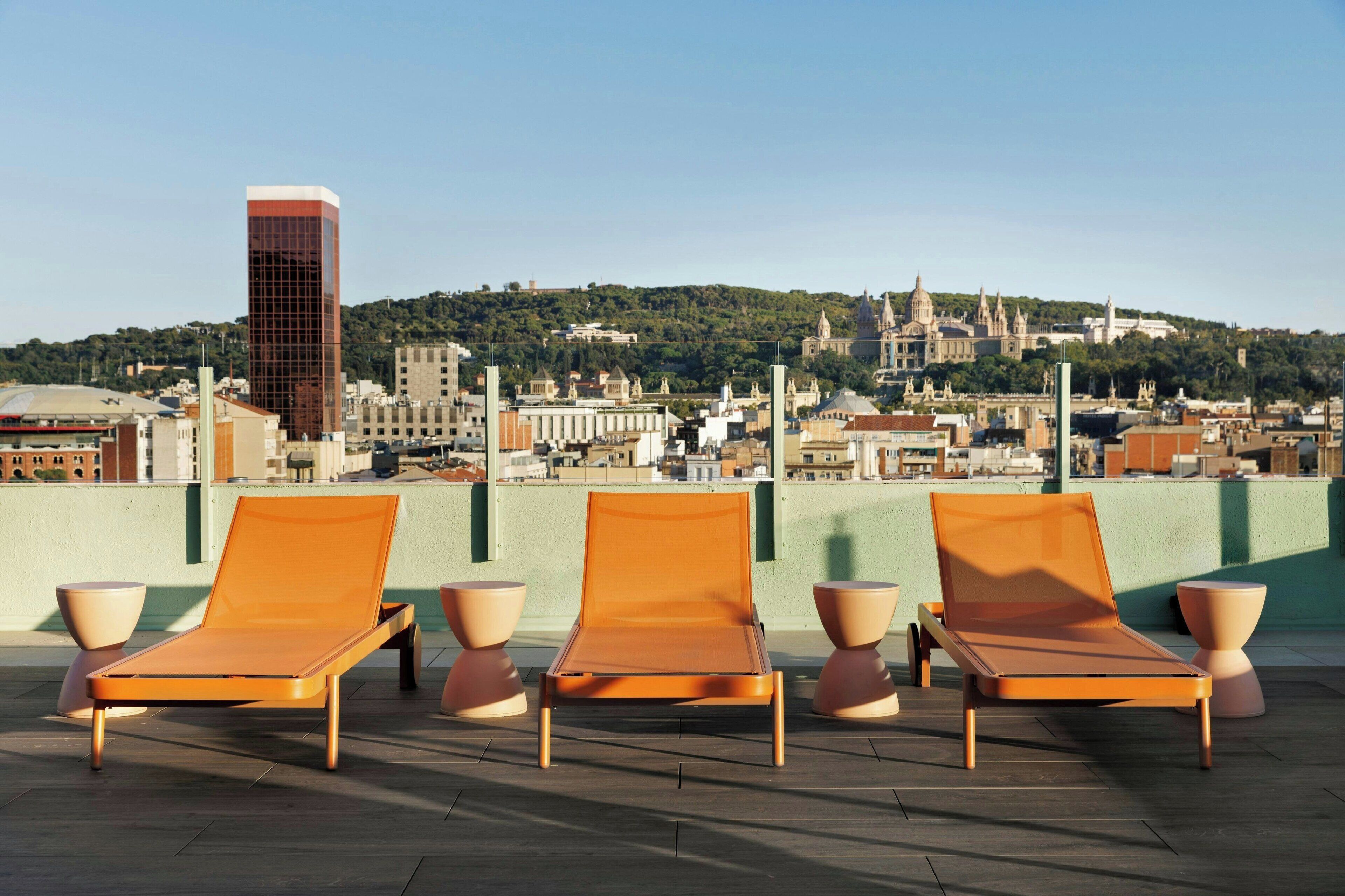 A rooftop terrace with three sun loungers and matching planters, overlooking a cityscape with historic buildings and a hill.