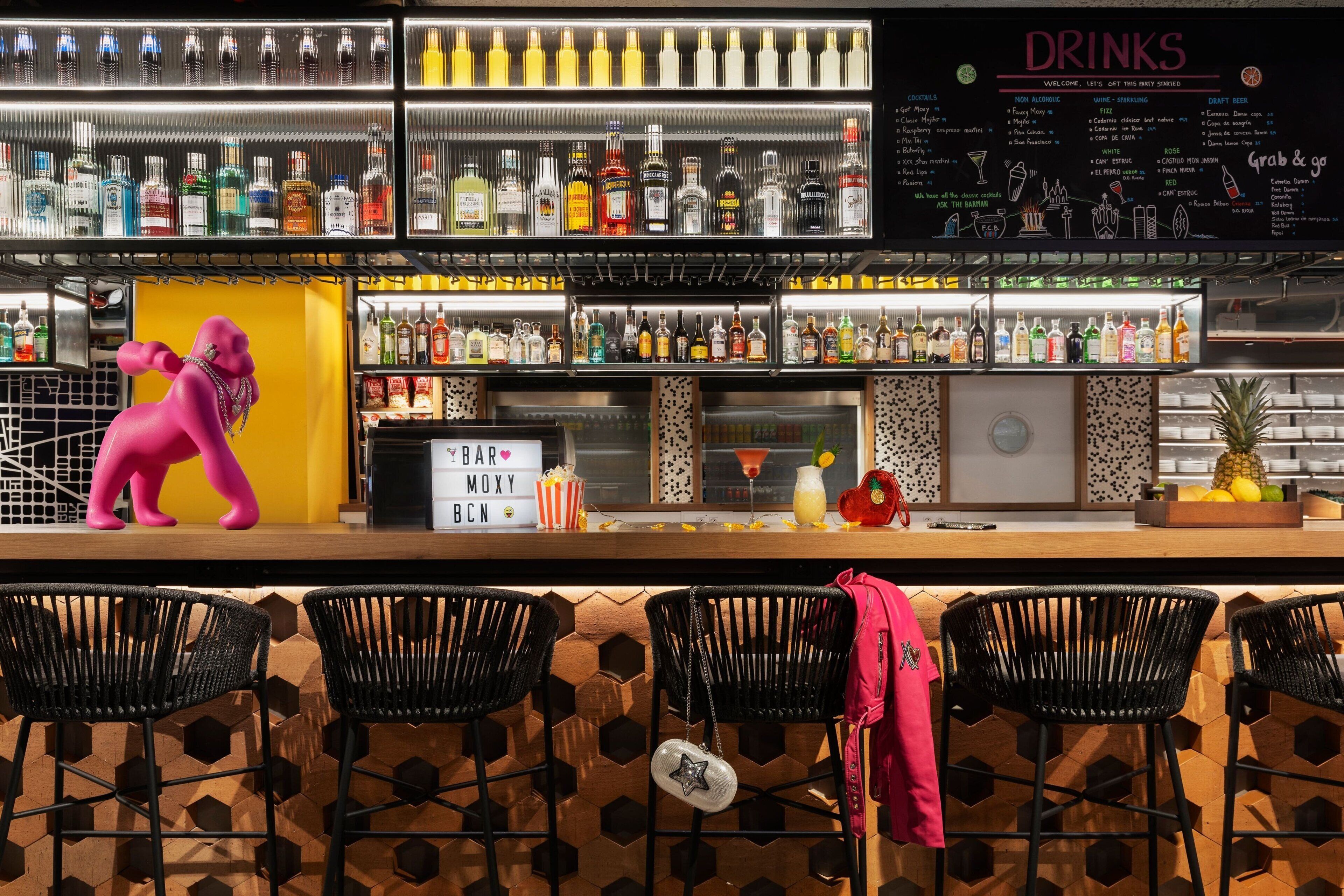 A bar area with a variety of liquor bottles, a pink elephant decoration, and black bar stools.