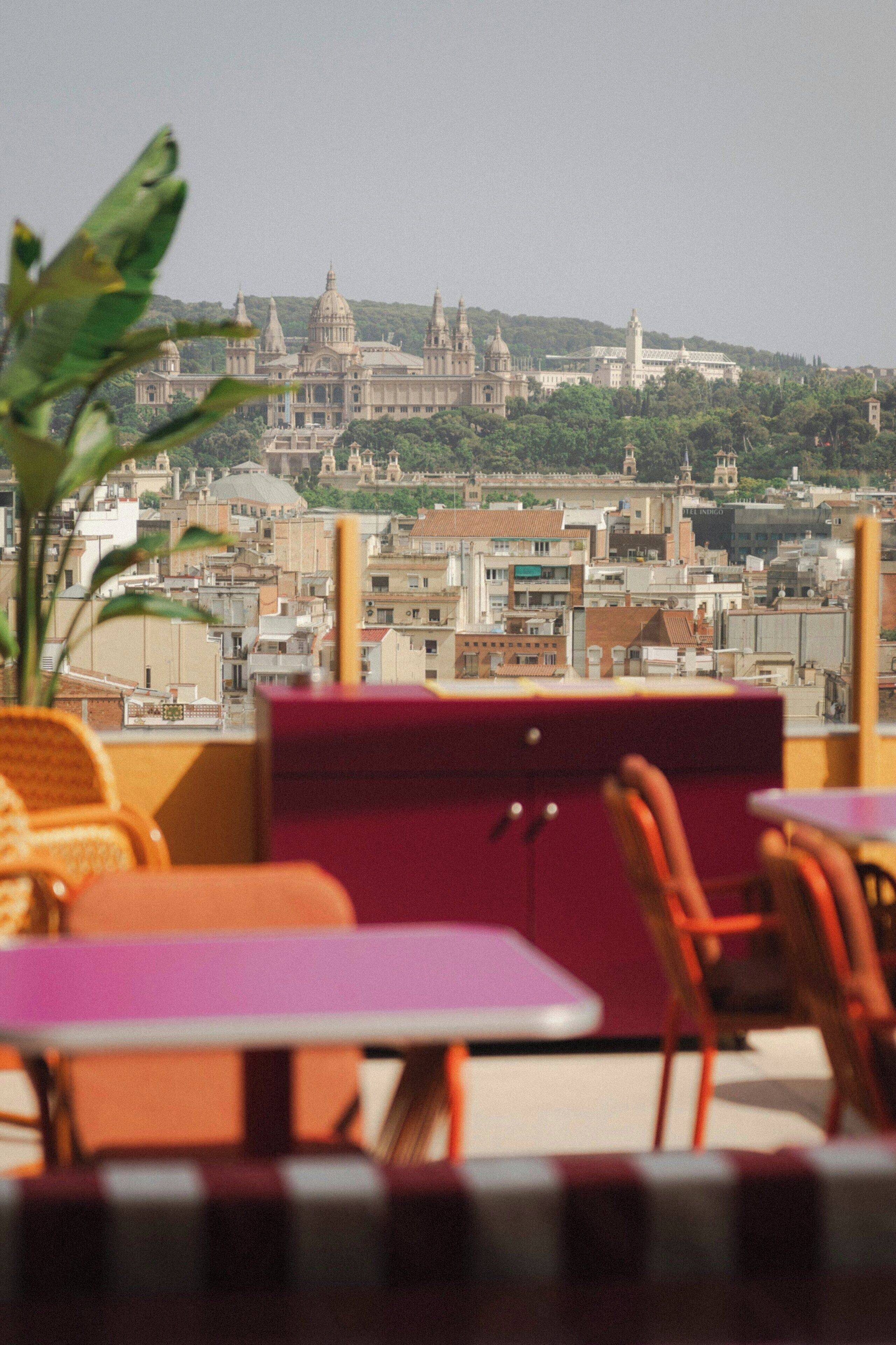 A view of a cityscape from a terrace with tables and chairs, overlooking a large historic building with domes and spires.