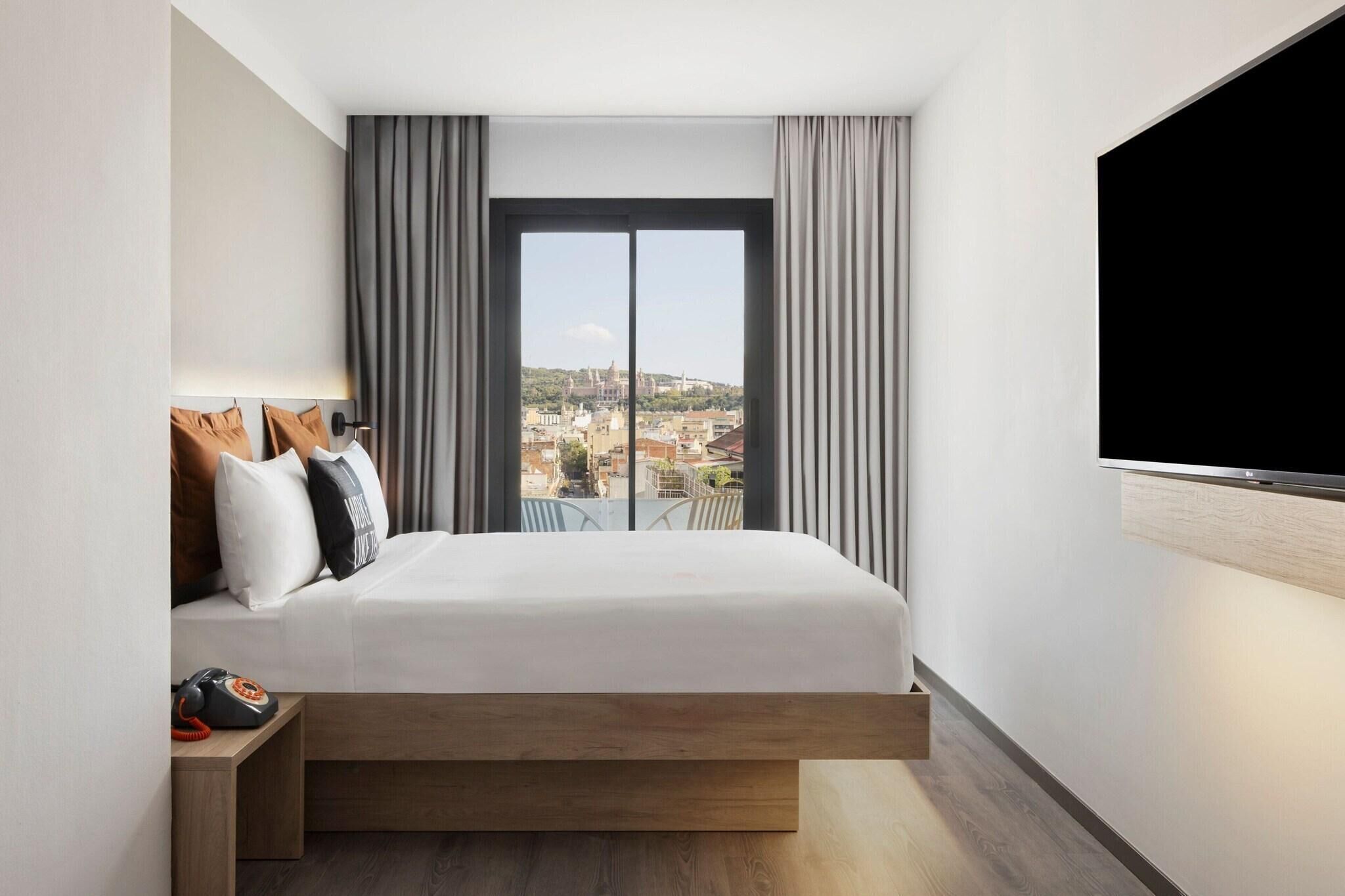 A modern hotel room with a large bed, a TV, and a view of the city.