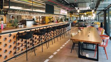 A modern bar area with a long counter, multiple bar stools, and a seating area with tables and chairs.