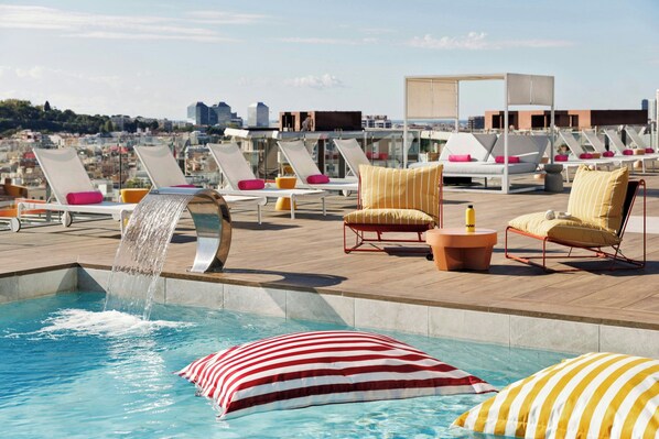 Un área de piscina en la azotea con sillones reclinables y una fuente.
