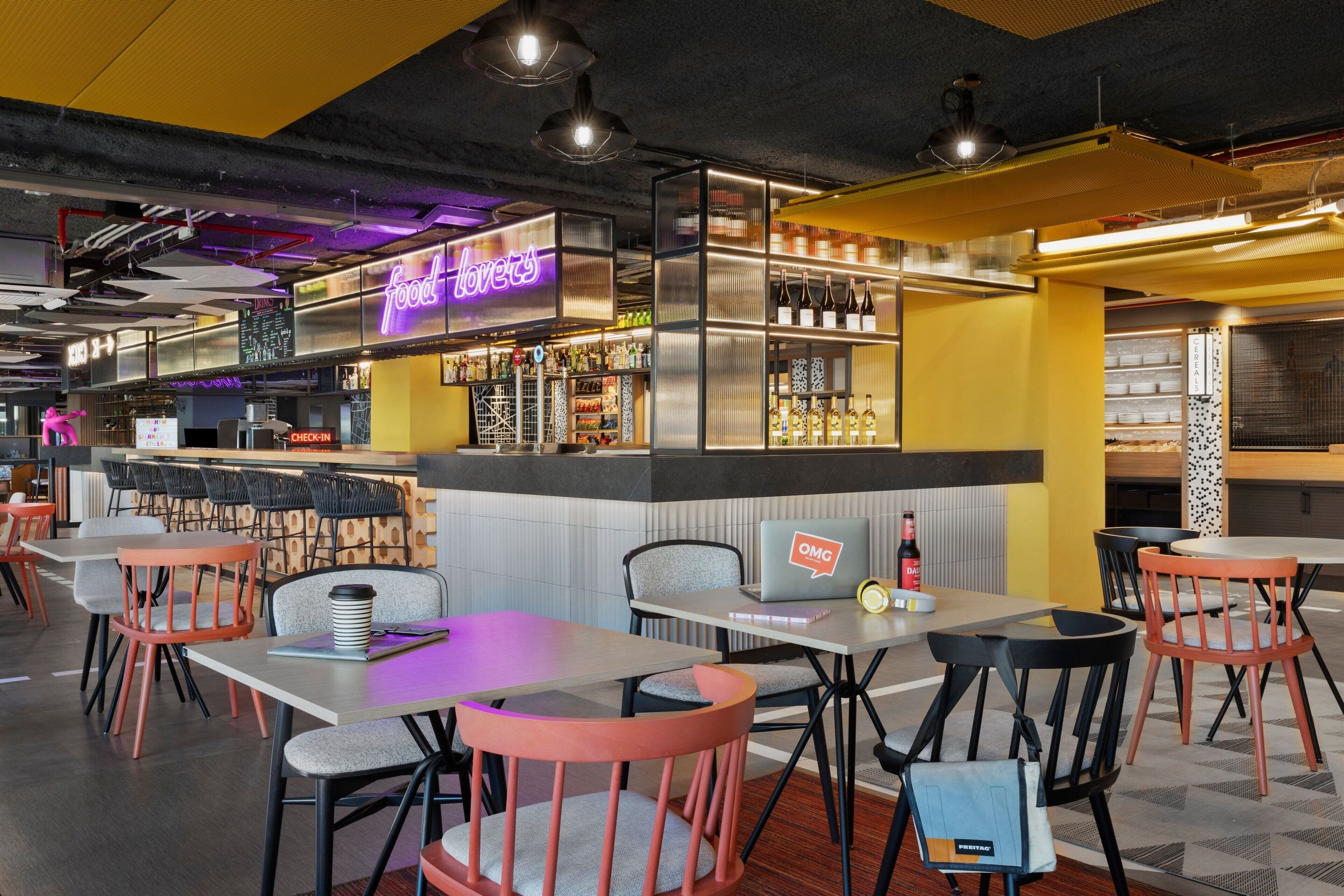 Un restaurante moderno con zona de bar, diferentes disposiciones de asientos y un letrero de neón.