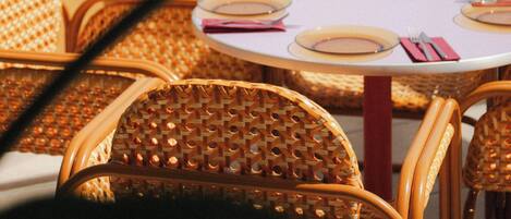 Una mesa puesta con platos, cubiertos y servilletas, con sillas de mimbre y vista a un paisaje urbano al fondo.