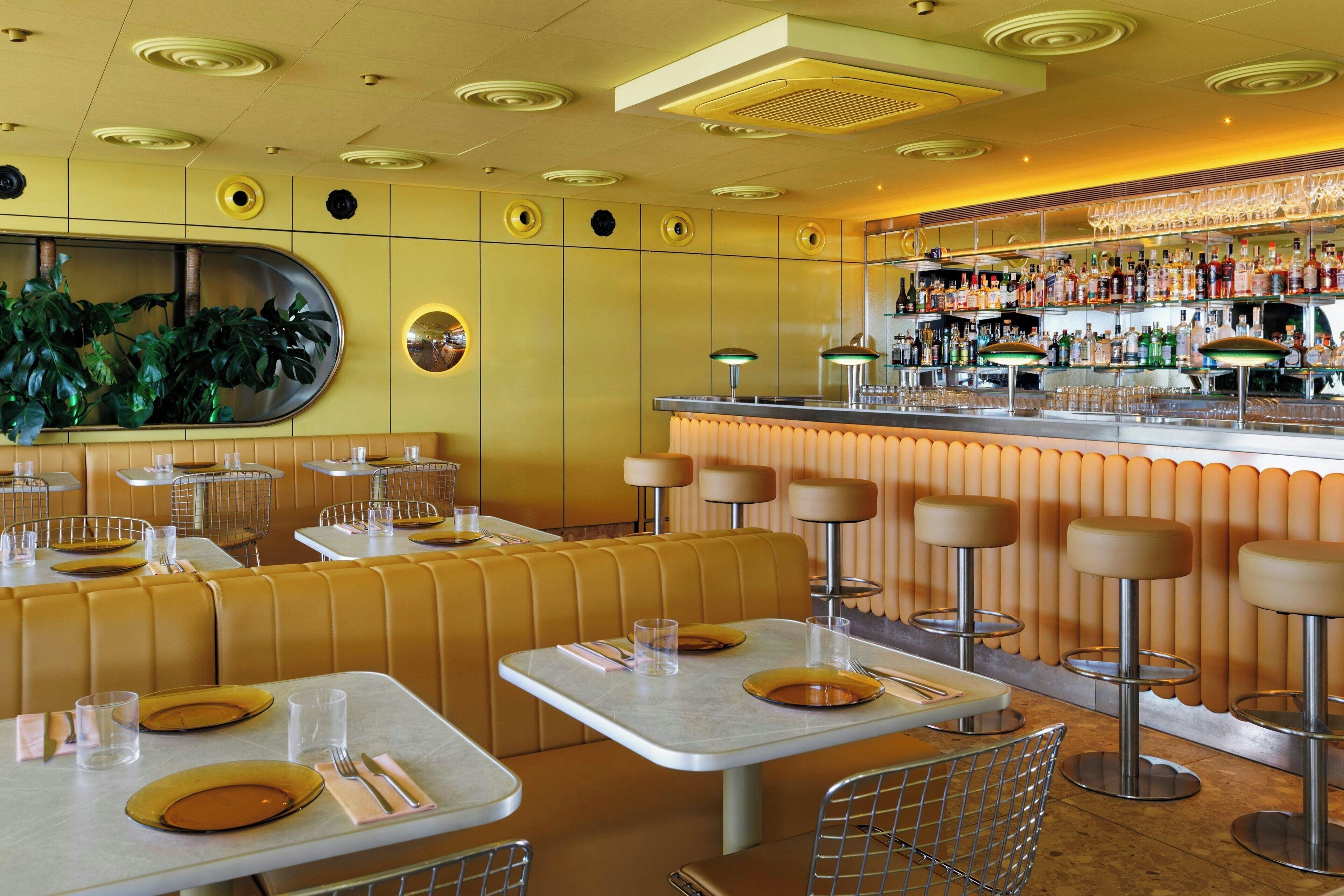 Un restaurante con cabinas y taburetes altos, una zona de bar con una variedad de botellas y un espejo grande en la pared.