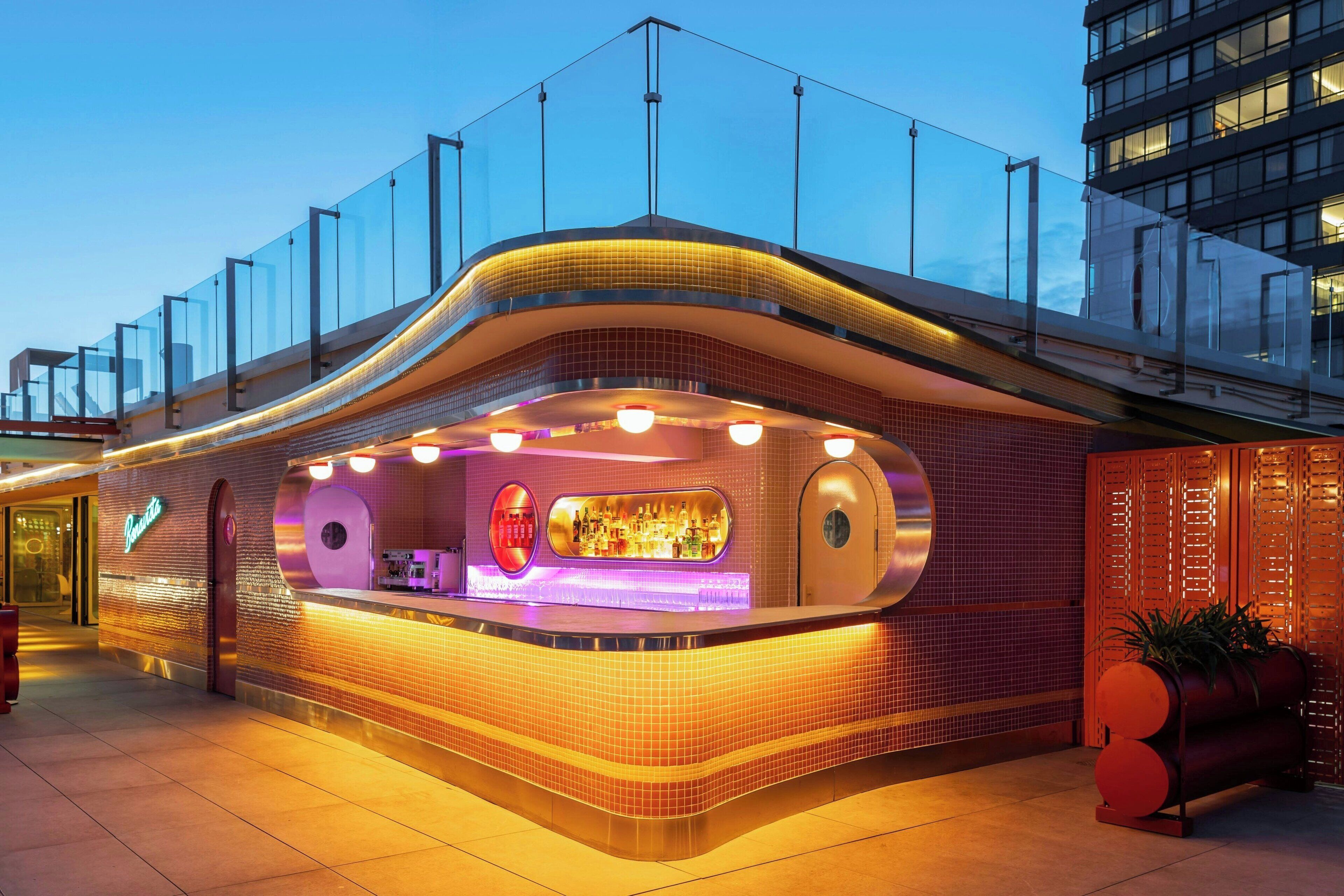 A modern bar with a curved design, glass railings, and a tiled facade.