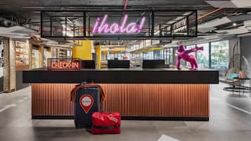 Una moderna recepción con un letrero de neón que dice 'hola', un cartel de 'registro' y una etiqueta de equipaje que dice 'Barcelona'.