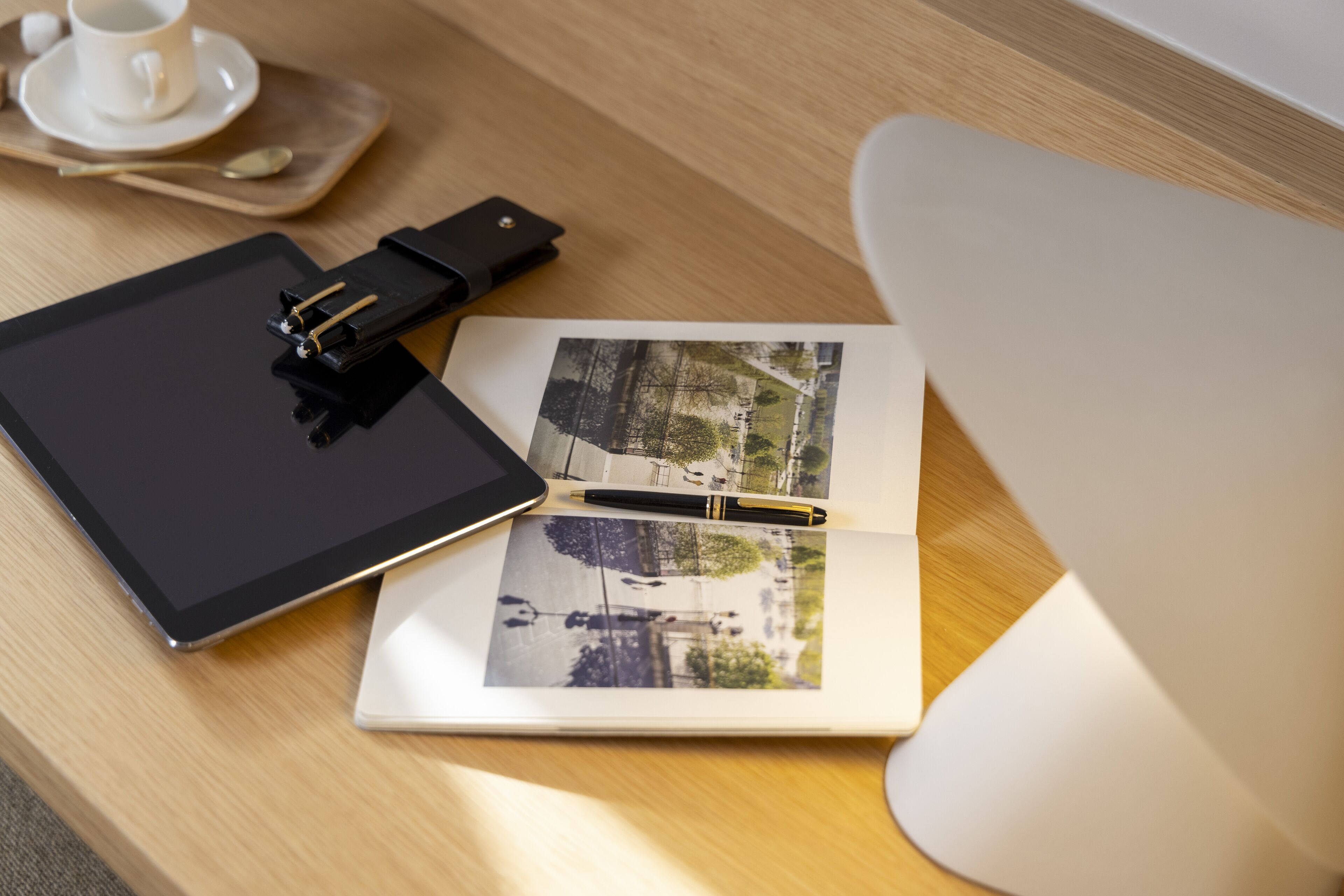 A wooden table with a tablet, a notebook, a pen, and a cup of coffee.