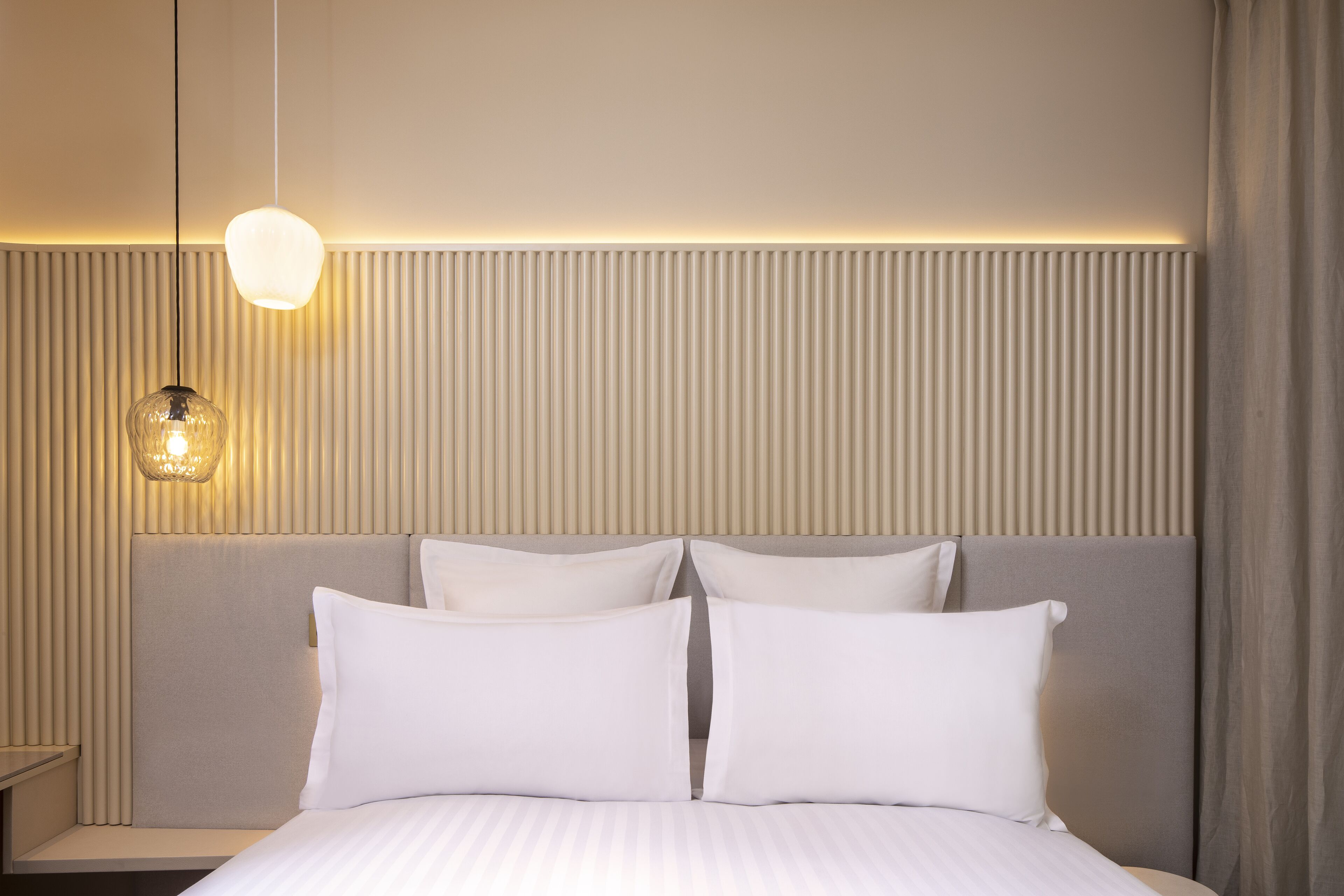 A hotel room with a large bed, a headboard with vertical lines, and a hanging light fixture.