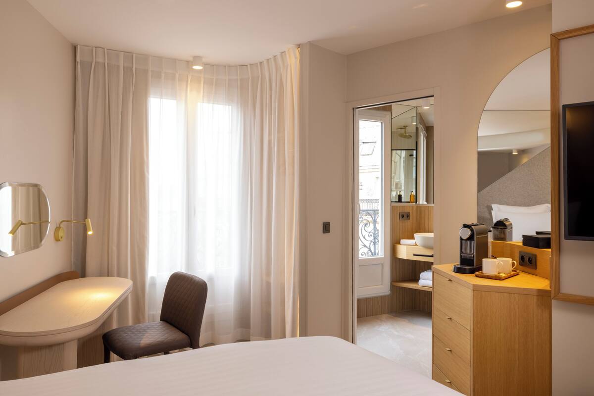 Une chambre d’hôtel équipée d’un lit, d’un bureau, d’une chaise, d’une commode, d’un miroir et d’une télévision.
