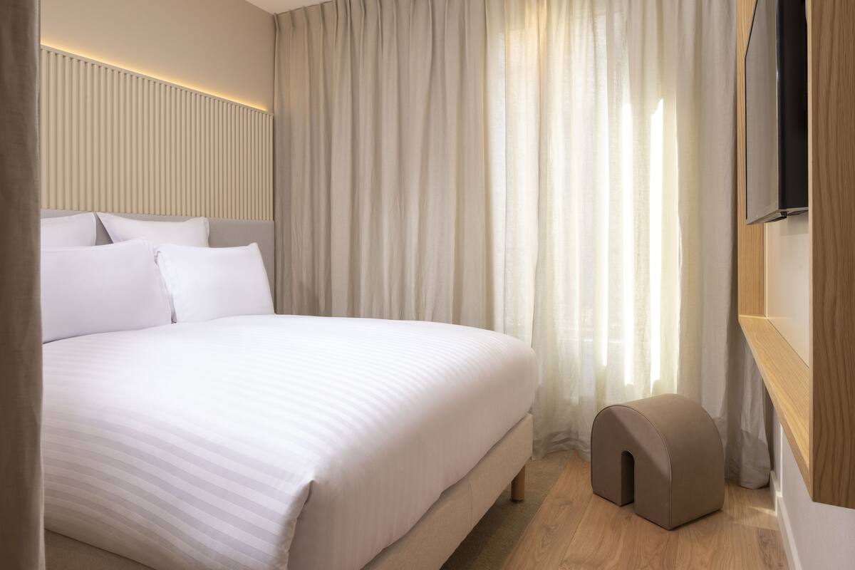 Une chambre d’hôtel moderne avec un grand lit, un plancher en bois et un téléviseur fixé au mur.